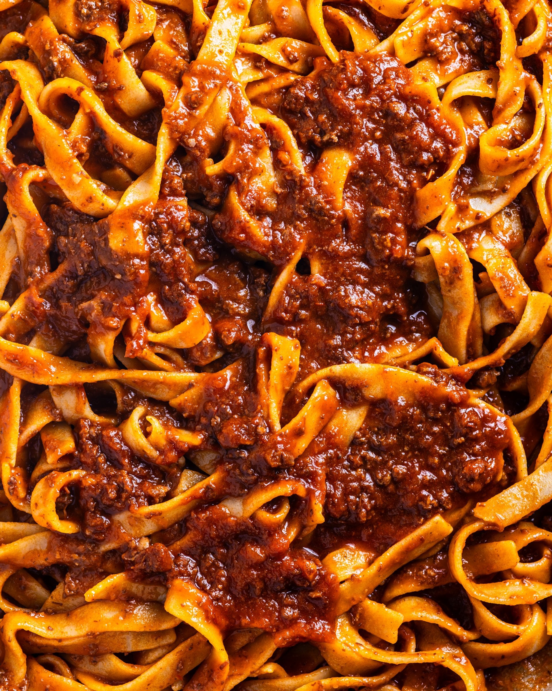 A close-up view of freshly cooked tagliatelle pasta coated in a rich, savory meat-based bolognese sauce.