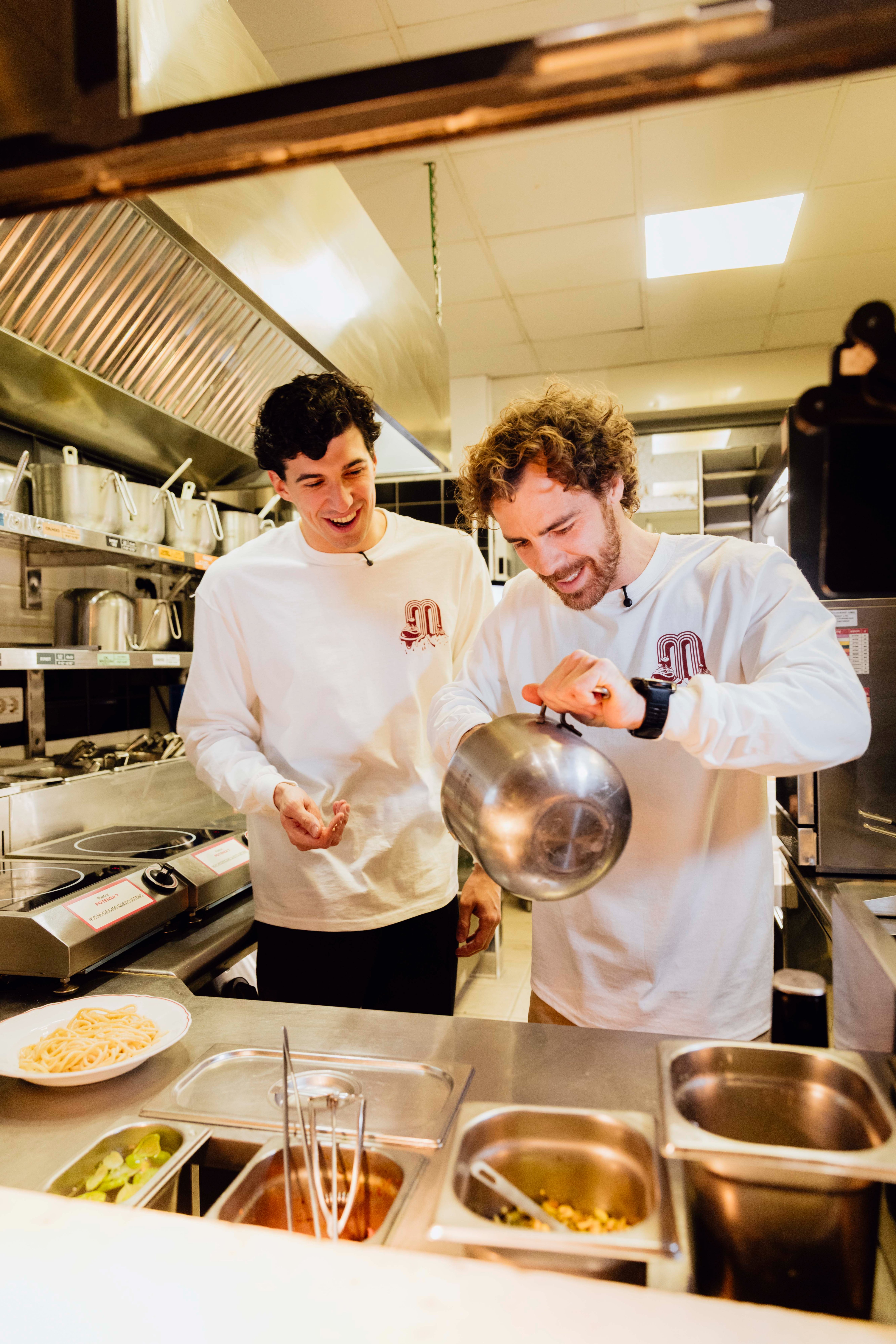 Two chefs in a professional kitchen prepare a meal together in a well-lit, collaborative atmosphere.