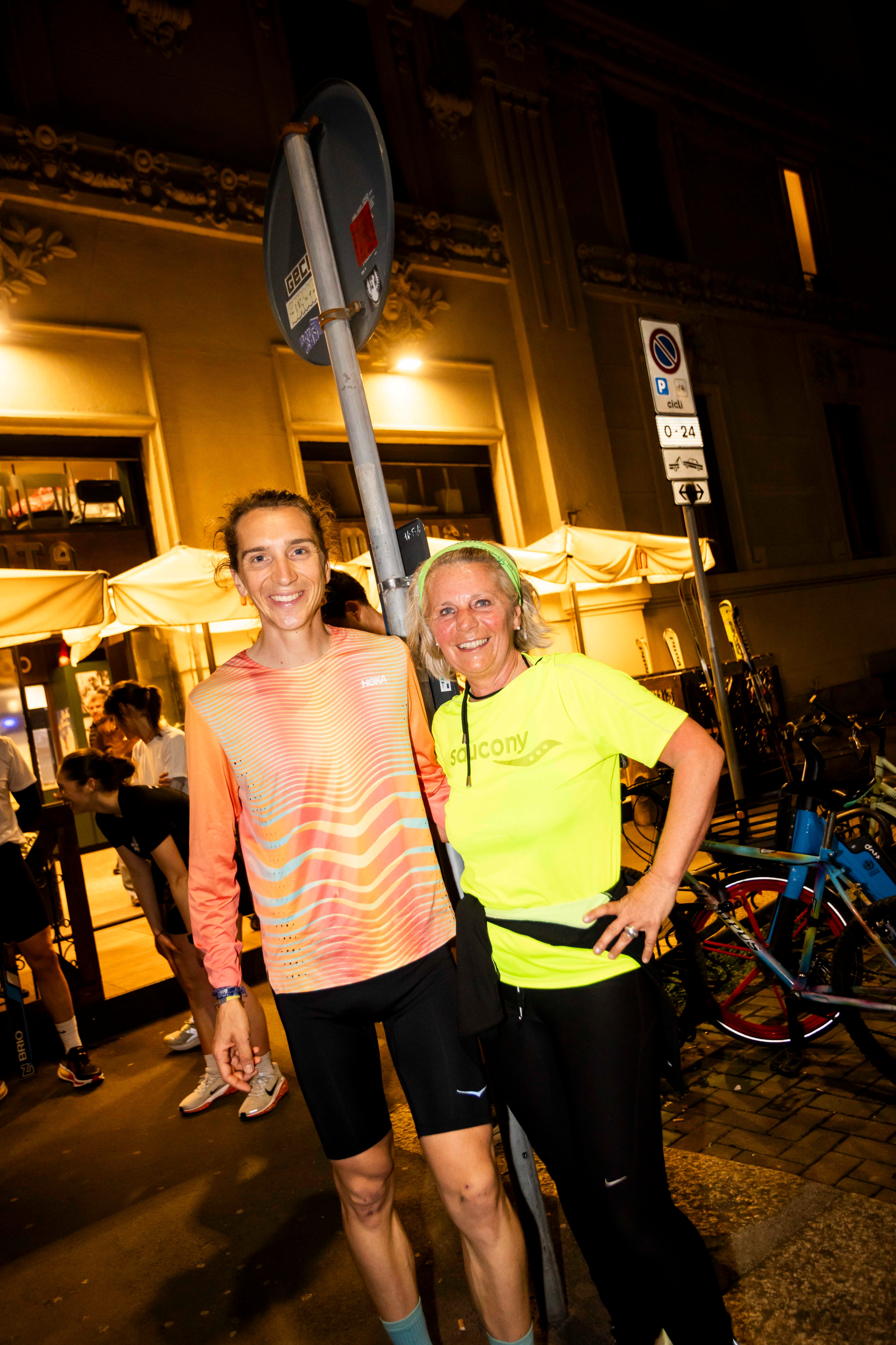 A smiling man and woman pose for a photo outside a restaurant at night.