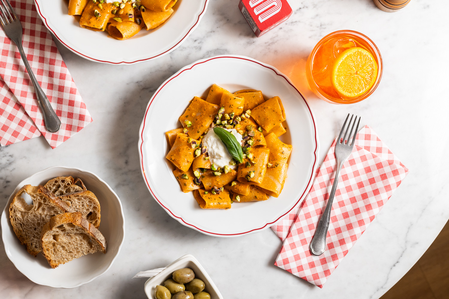 A top-down view of a delicious pasta dish served with ricotta, pistachios, and a refreshing orange cocktail on a marble table.