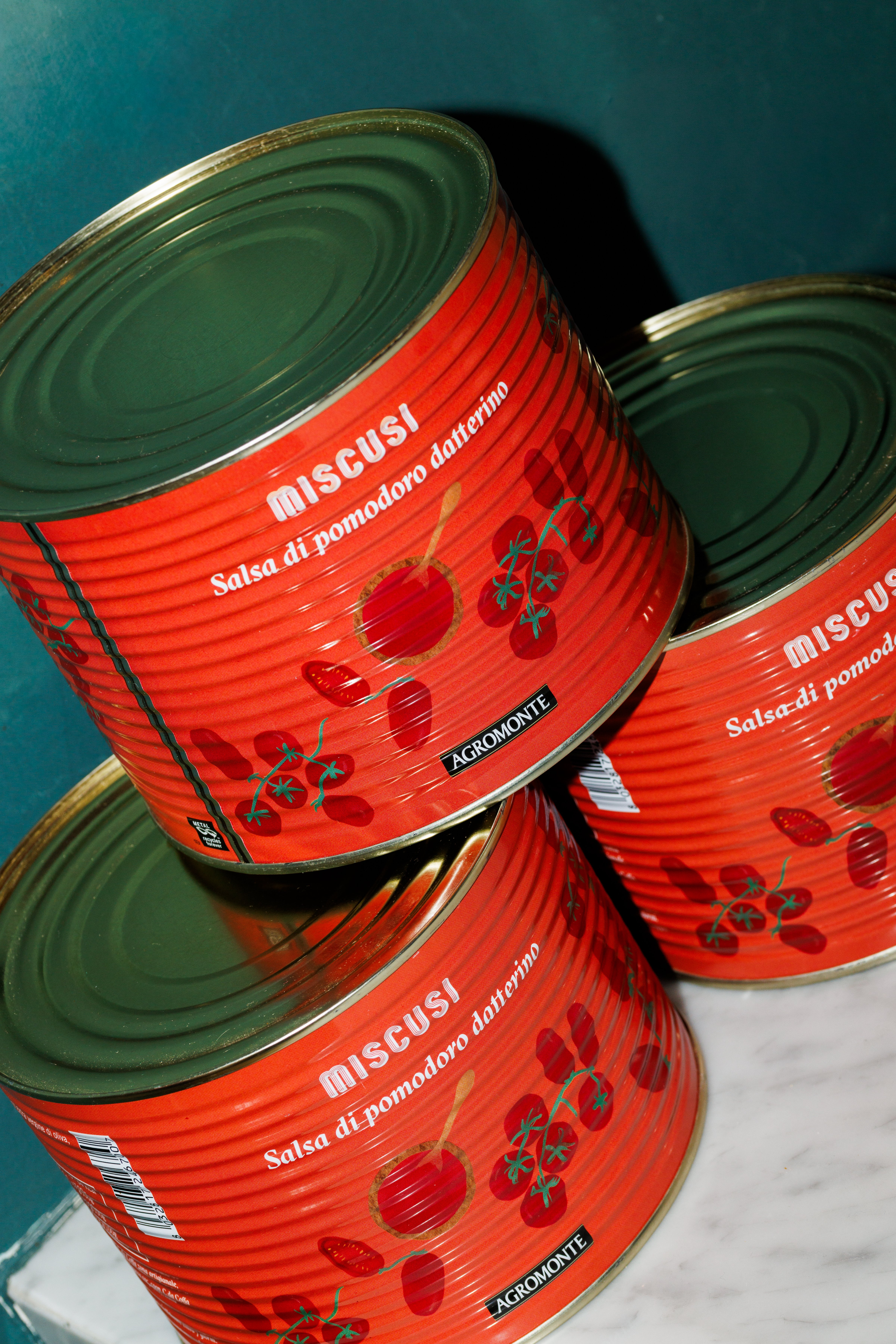 Three stacked metal cans of Miscusi datterino tomato sauce are displayed against a dark background.