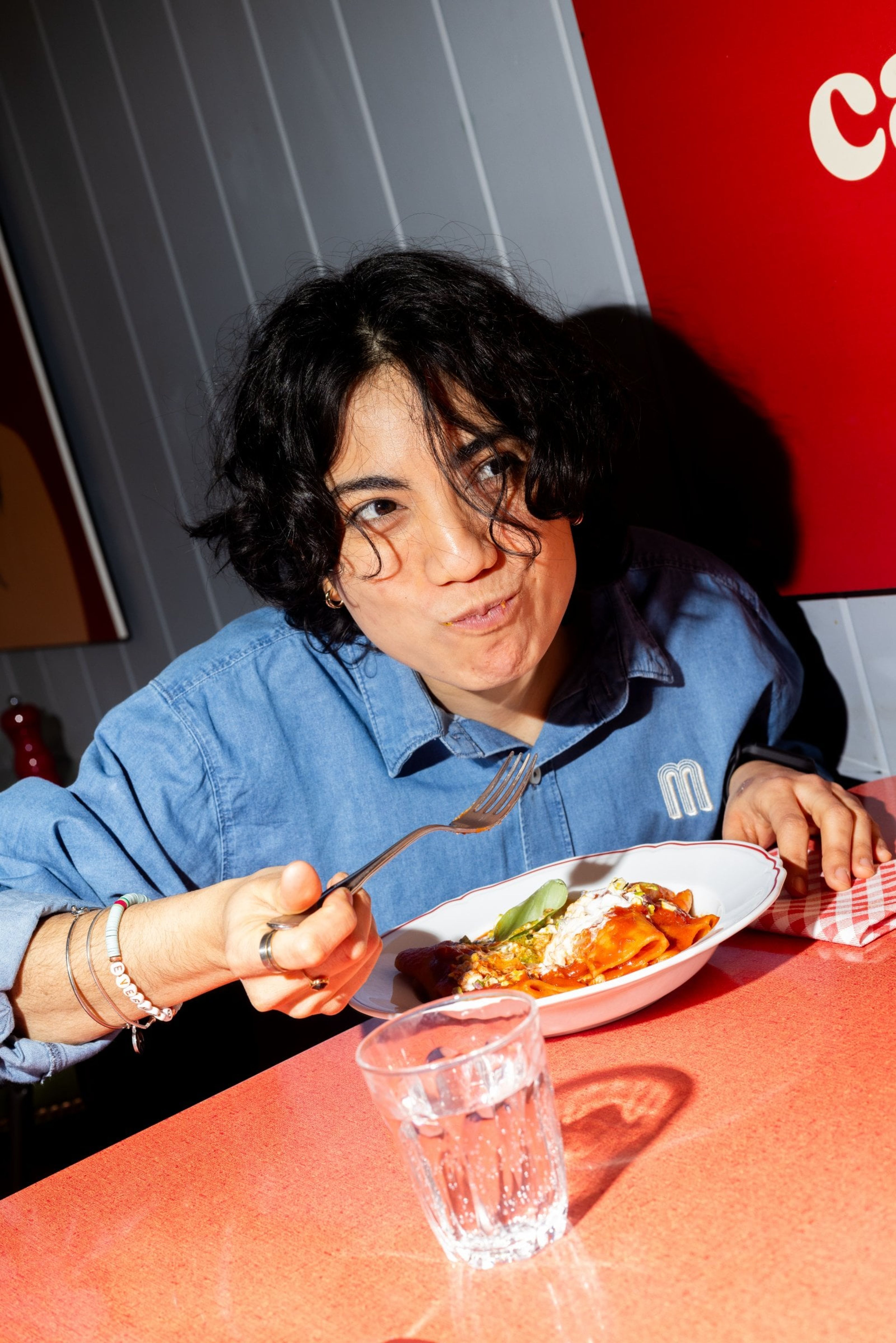 A person enjoys a plate of pasta with tomato sauce in a brightly lit, casual restaurant setting.