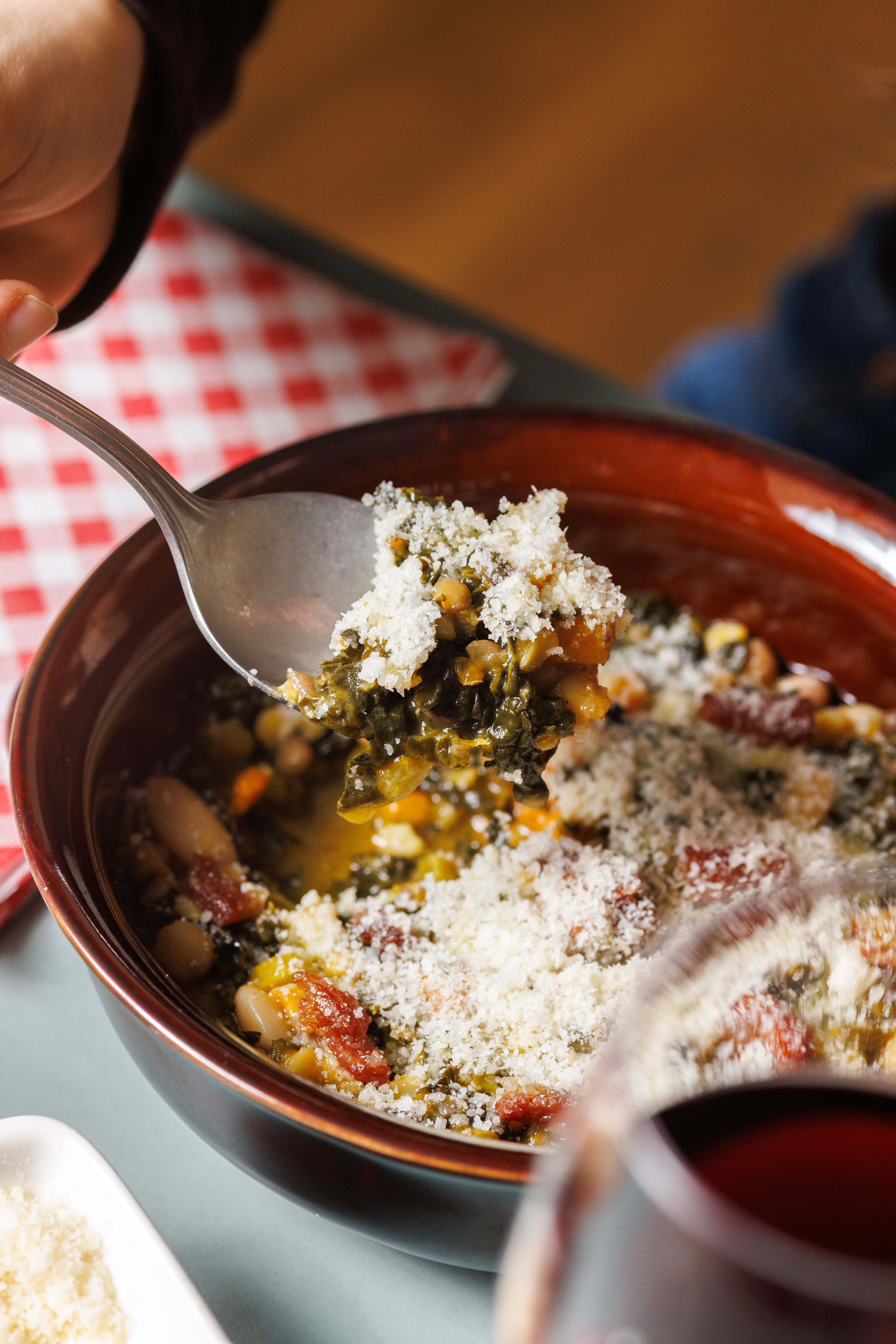 A close-up of a spoonful of hearty vegetable and bean soup topped with grated parmesan cheese.