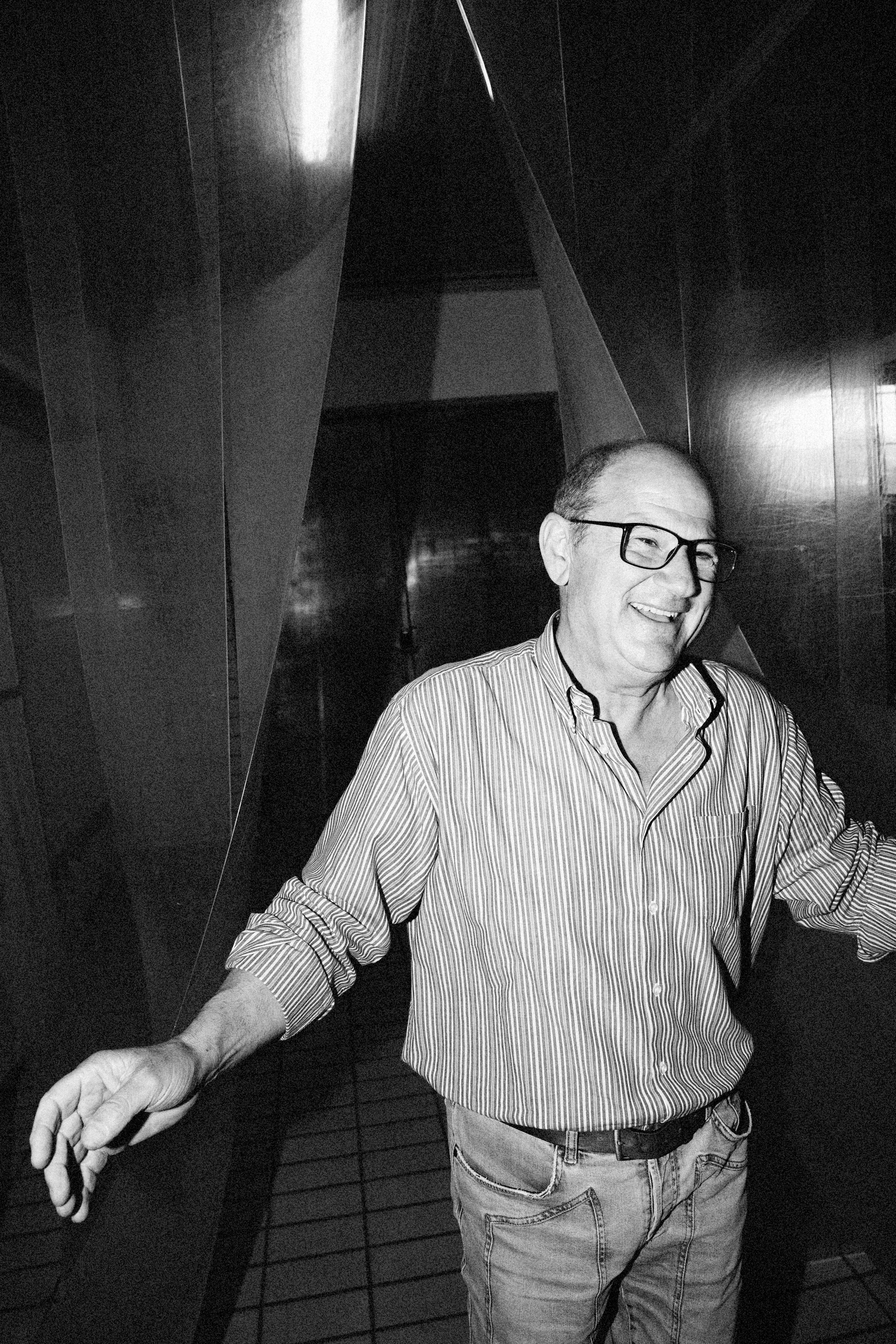 A man in a striped shirt smiles warmly in a dimly lit, modern interior space.