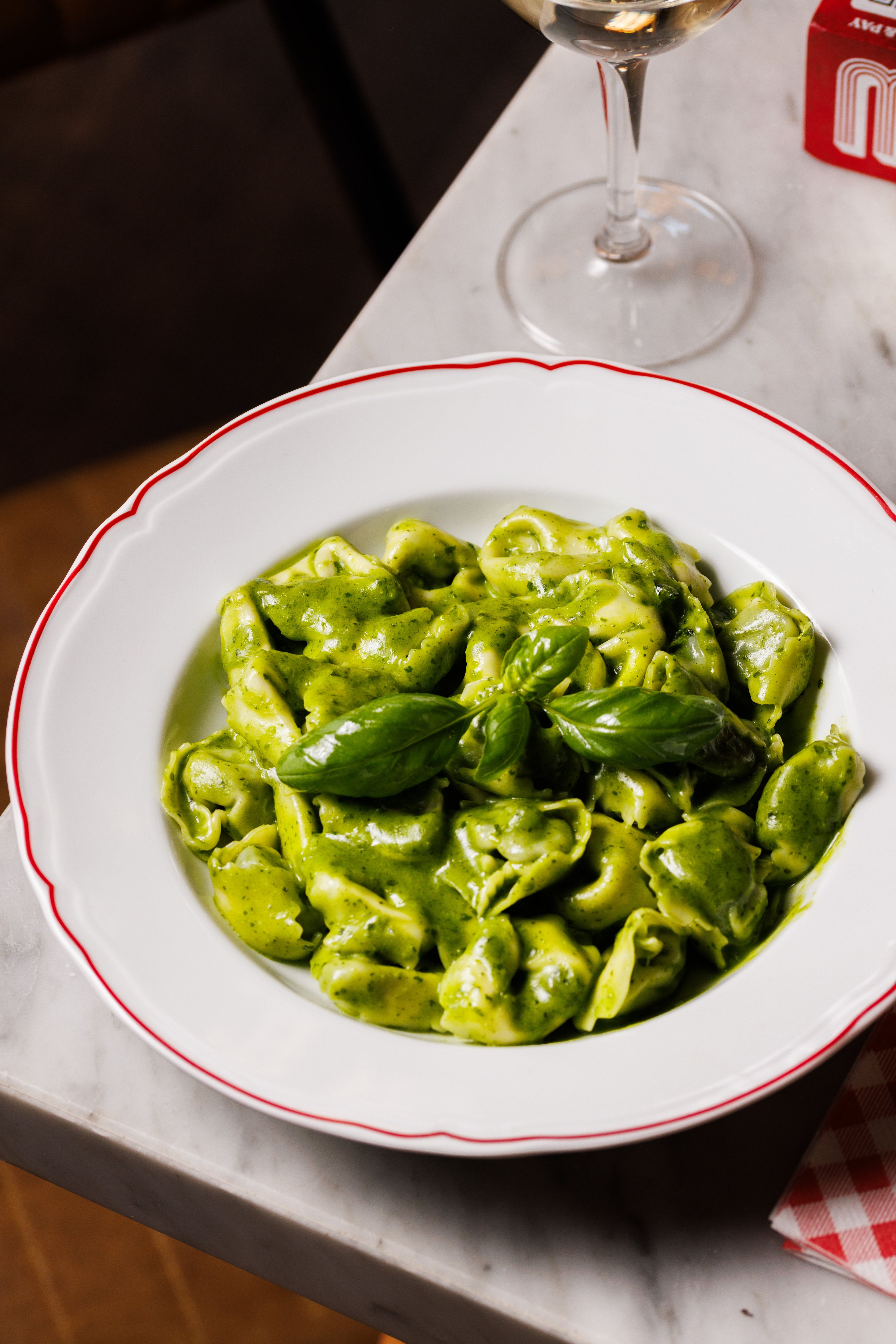 A plate of tortellini pasta coated in a vibrant green pesto sauce and garnished with fresh basil leaves.