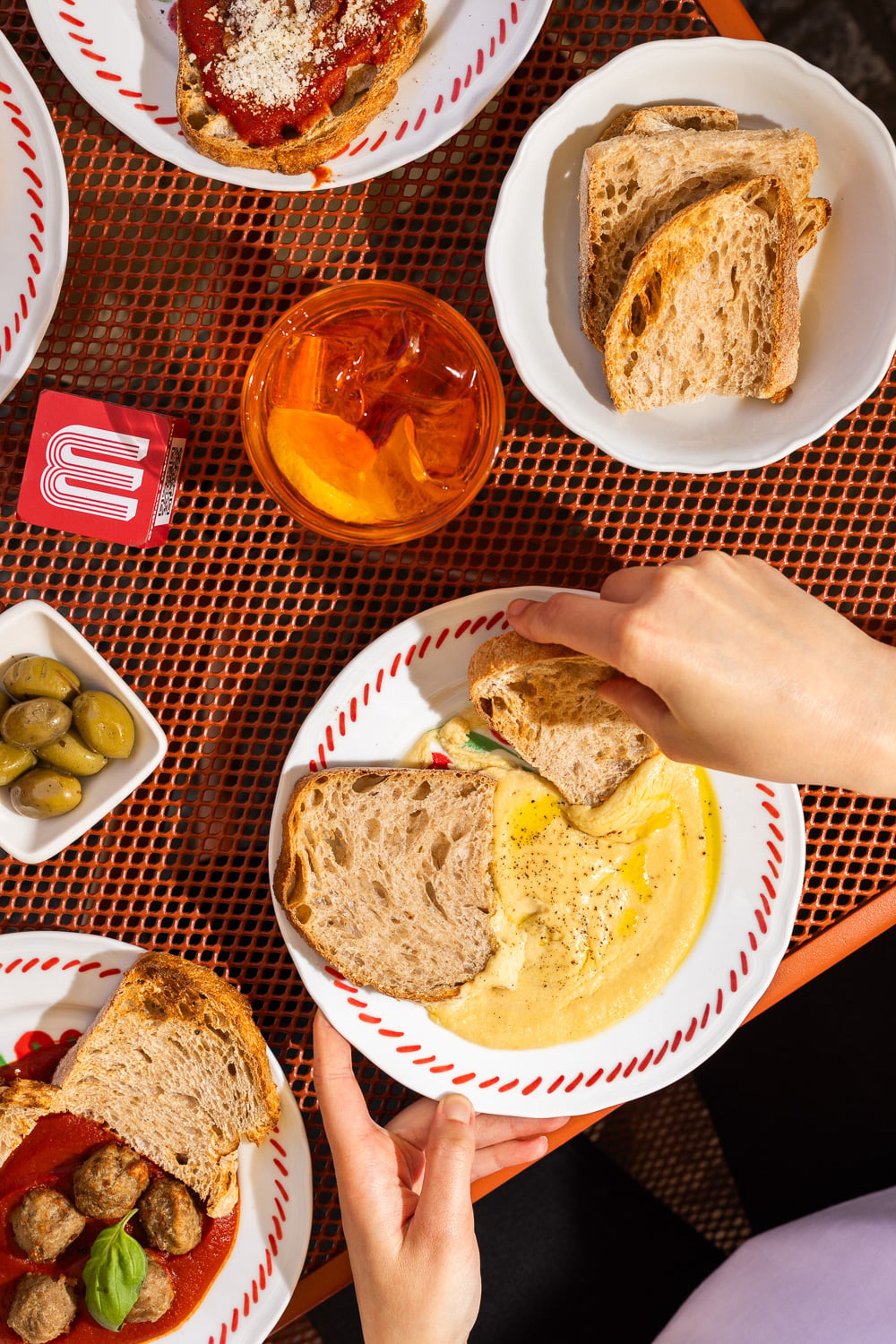 A top-down view of a vibrant outdoor table featuring various appetizers, toasted bread, and a refreshing cocktail.