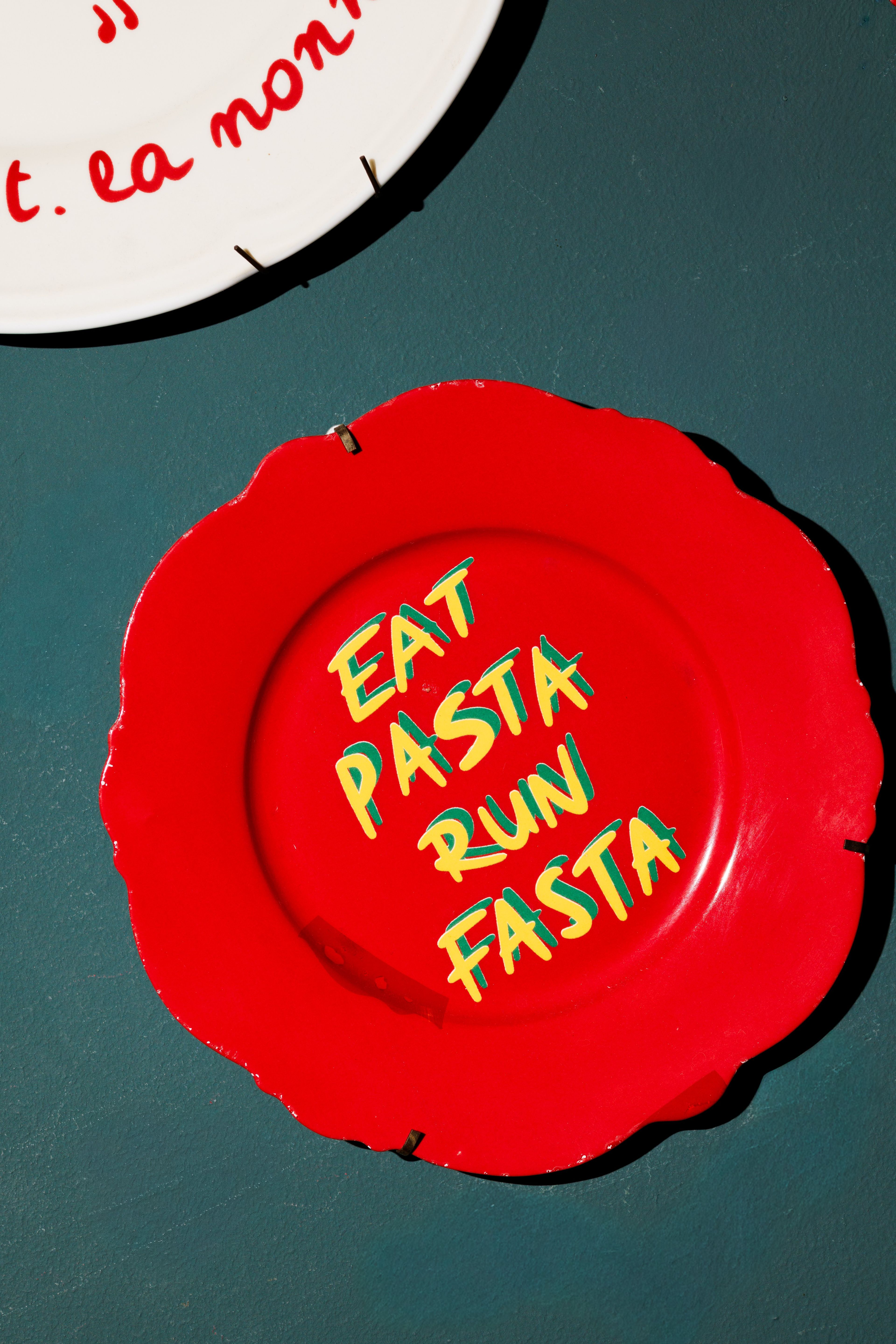 A red decorative plate with the phrase 'EAT PASTA RUN FASTA' displayed on a dark wall.