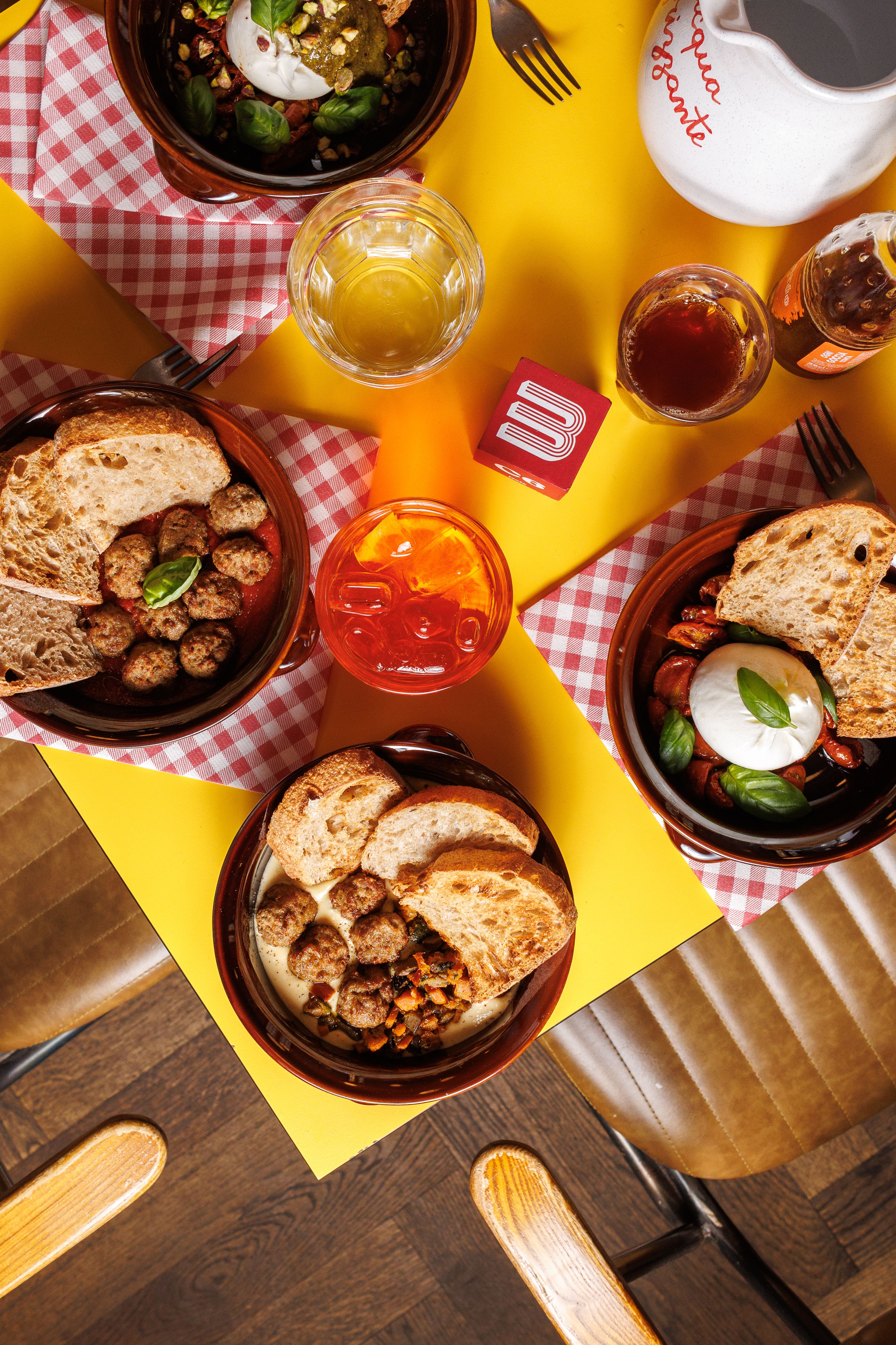 A top-down view of a vibrant restaurant table featuring several bowls of Italian-inspired dishes, bread, and drinks.