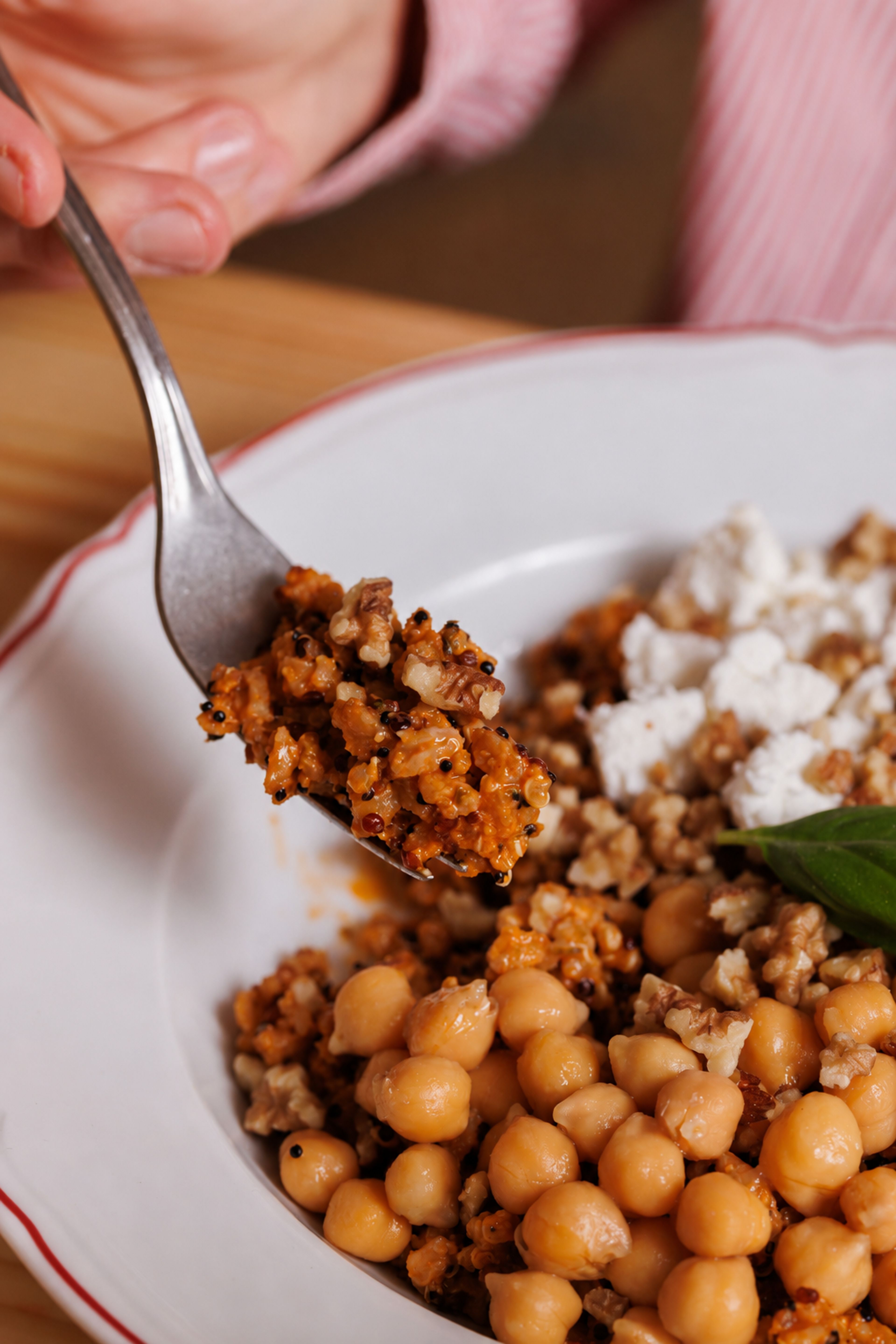 A close-up view shows a fork lifting a portion of a nutritious grain and chickpea salad topped with crumbled feta cheese.