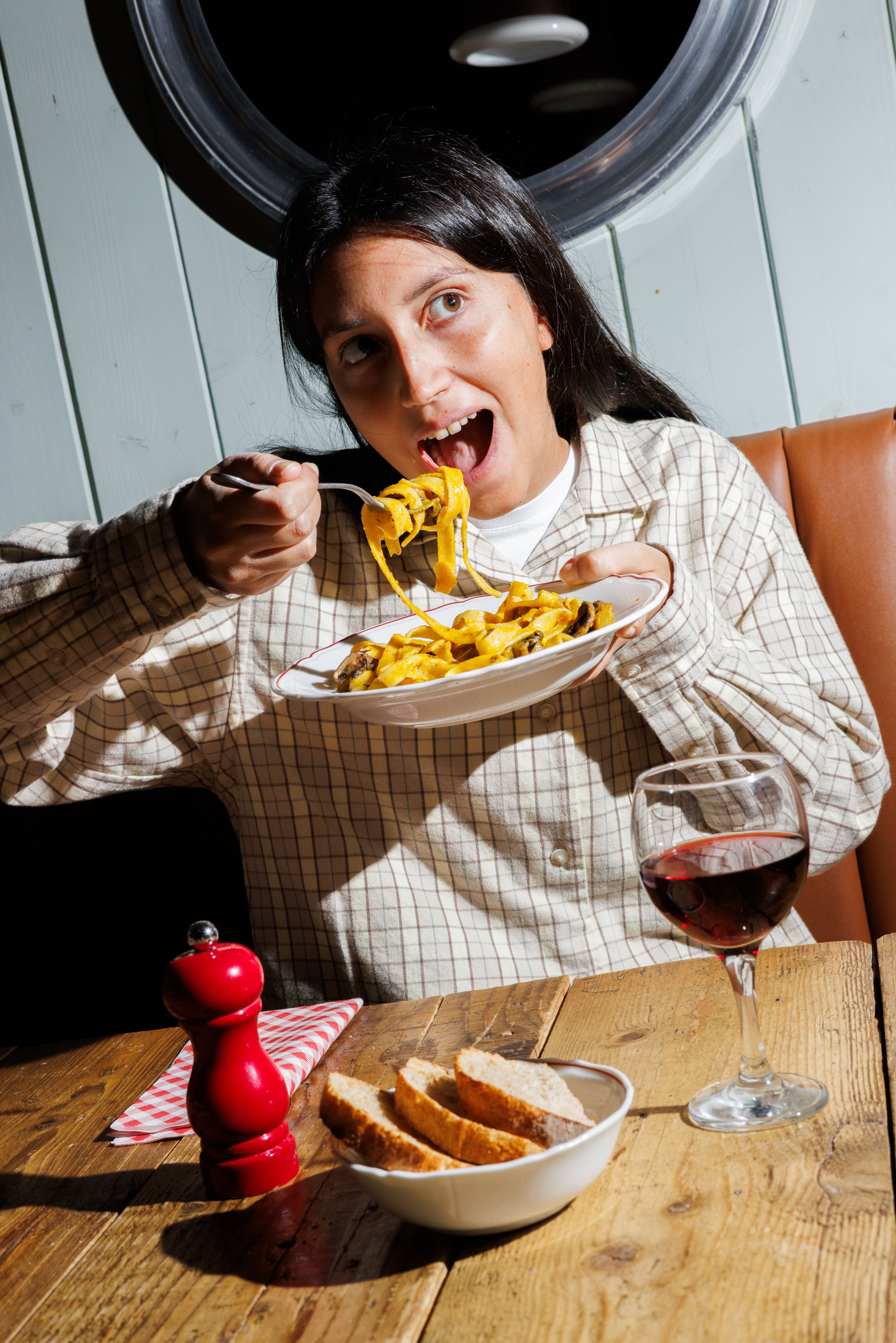 A person enjoys a plate of pasta with mushrooms in a warmly lit restaurant setting.