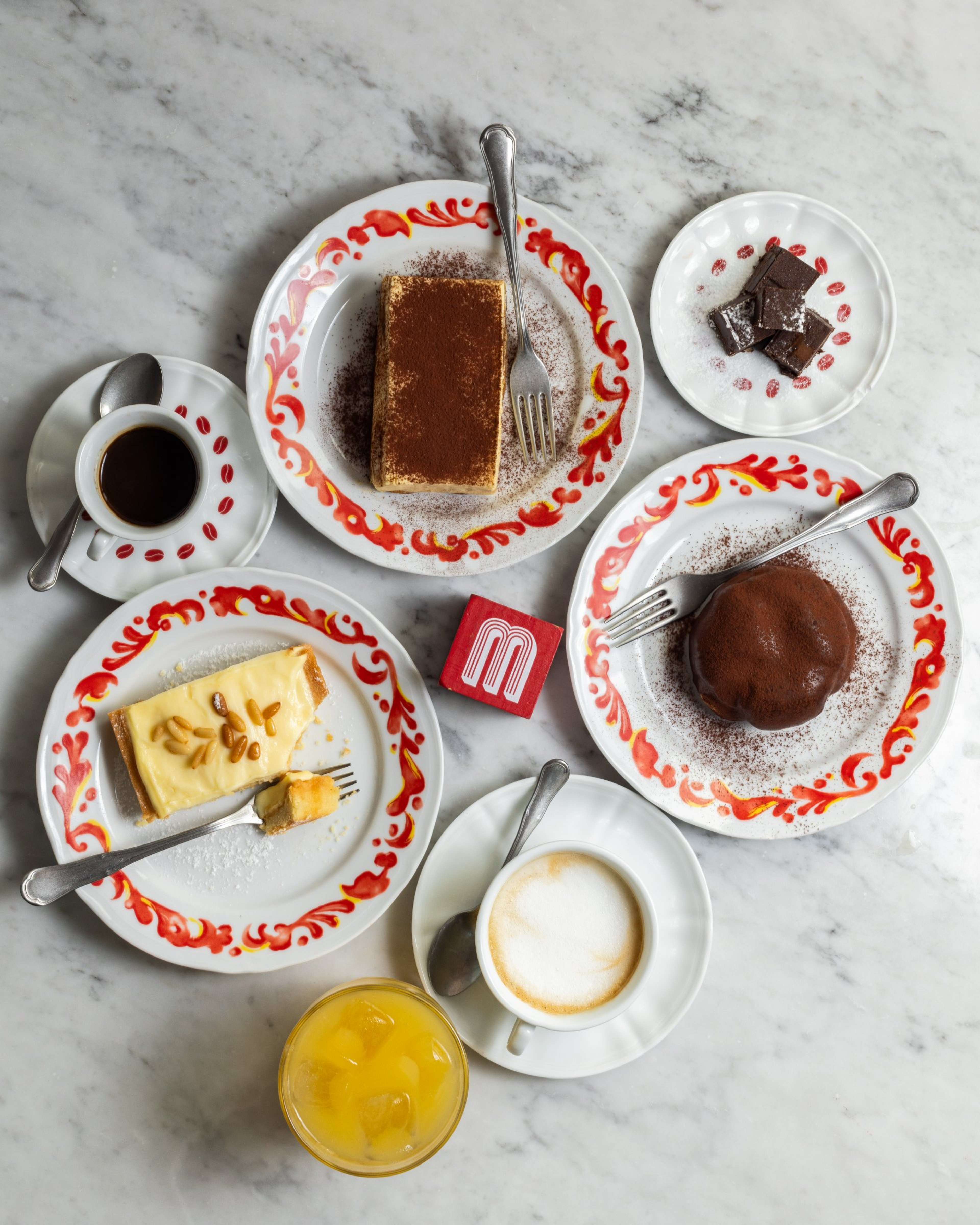 A top-down view of a marble table featuring an assortment of Italian desserts, coffee, and juice.