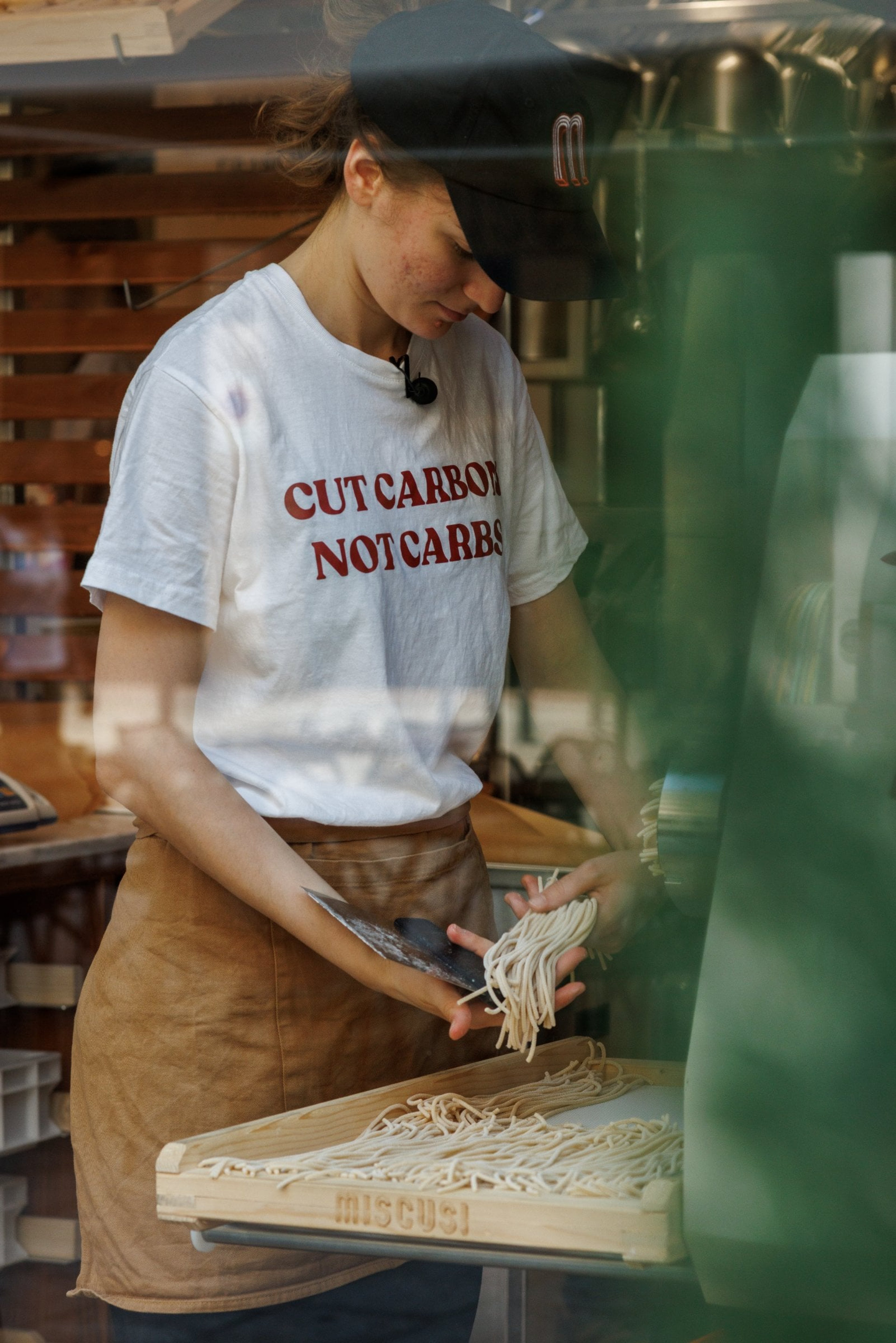A person wearing a slogan t-shirt prepares fresh pasta in a brightly lit kitchen.