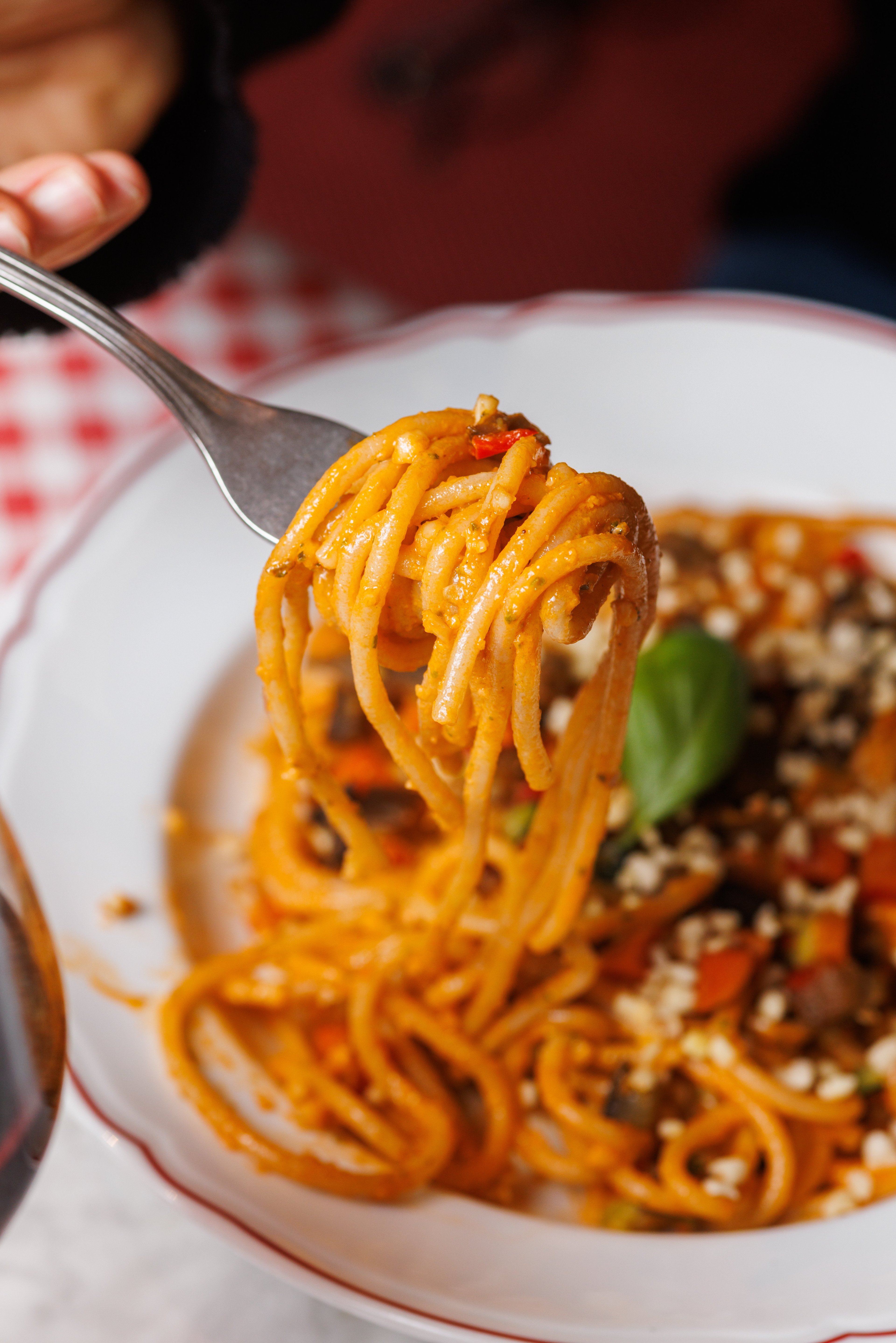 A close-up shot captures a fork lifting a portion of vibrant, sauce-coated spaghetti from a plate at a restaurant.
