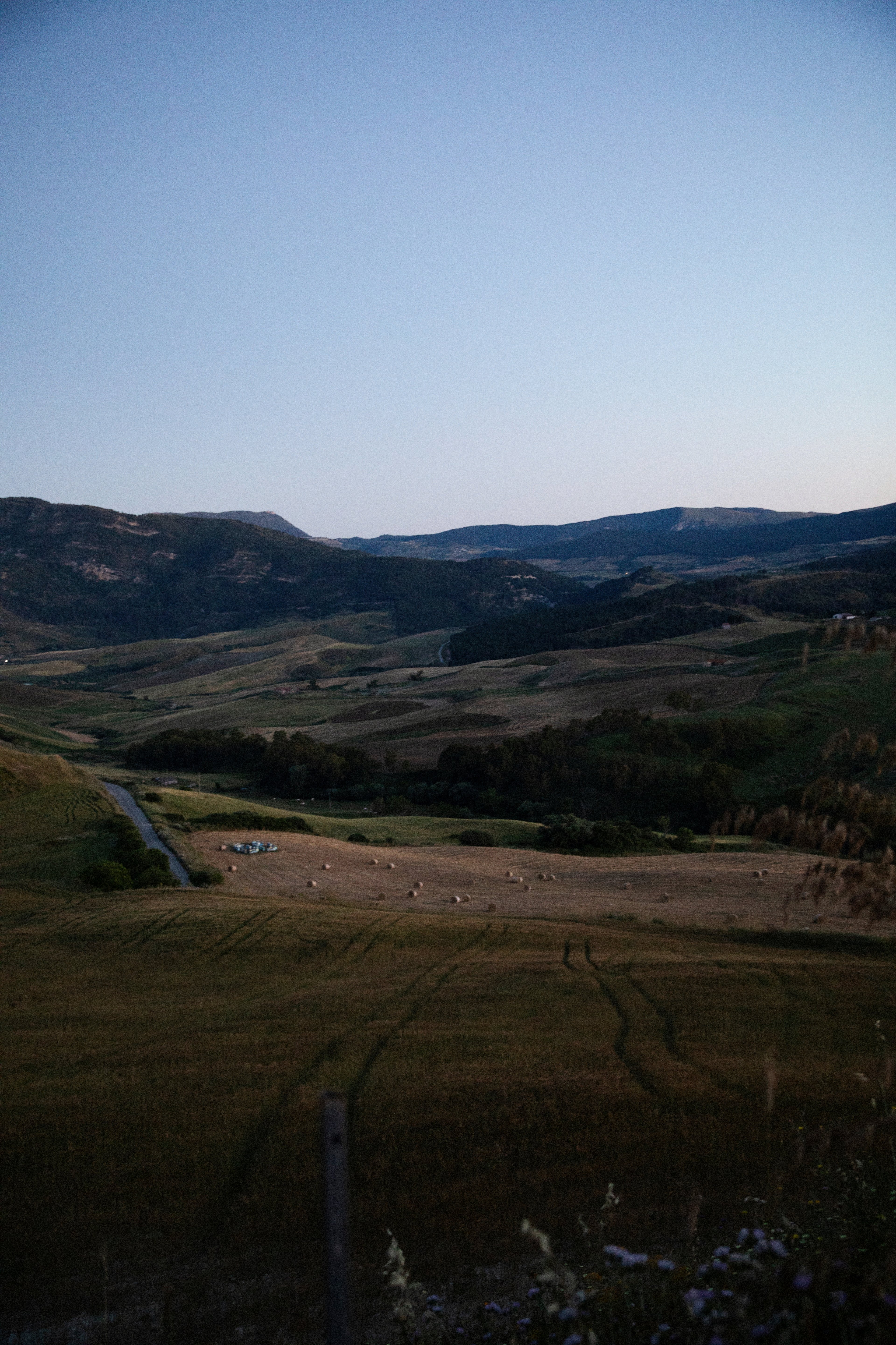 A serene landscape view of rolling hills and fields with hay bales under a clear twilight sky.