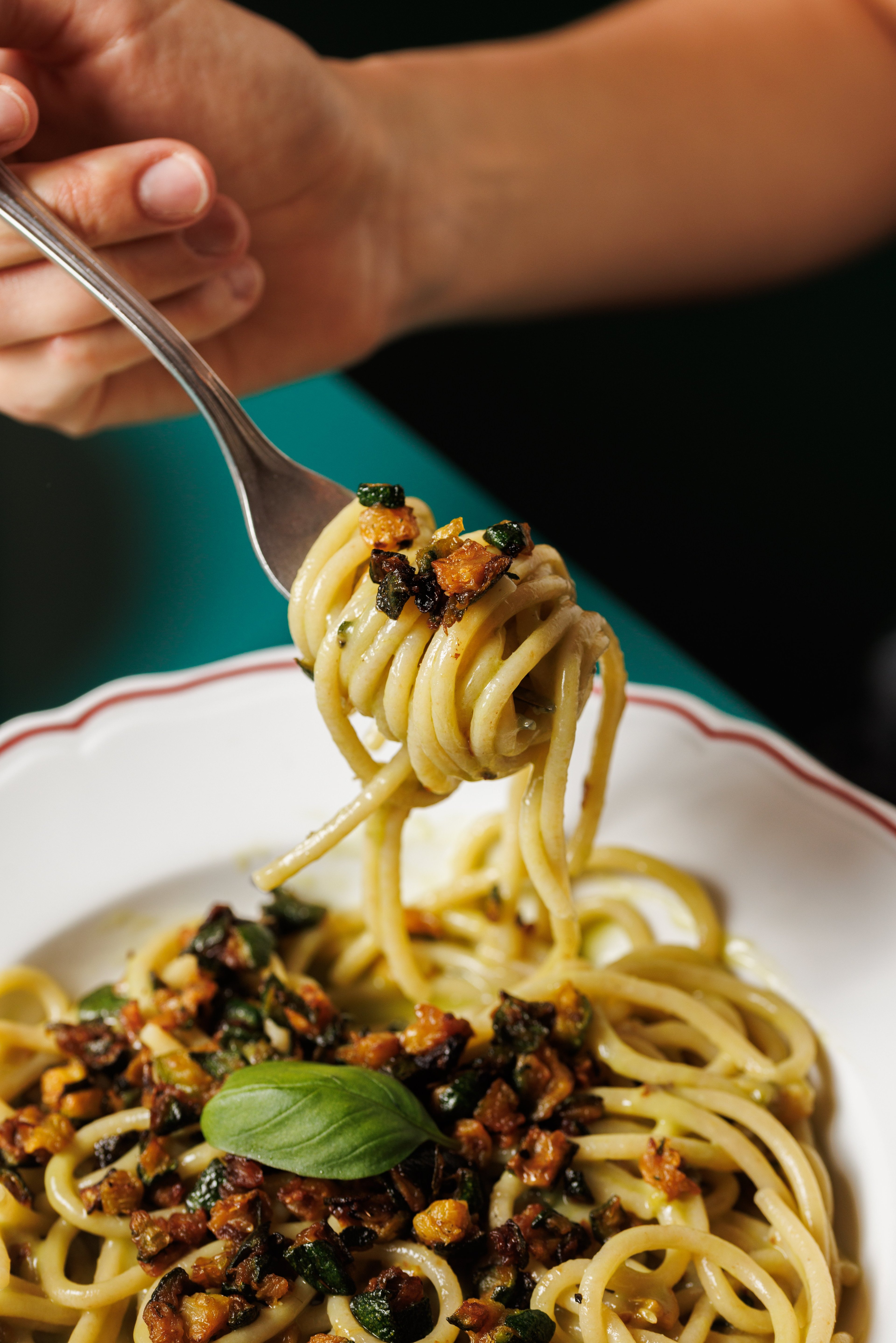 A close-up shot captures a fork lifting a portion of spaghetti tossed with sautéed zucchini and herbs from a white plate.