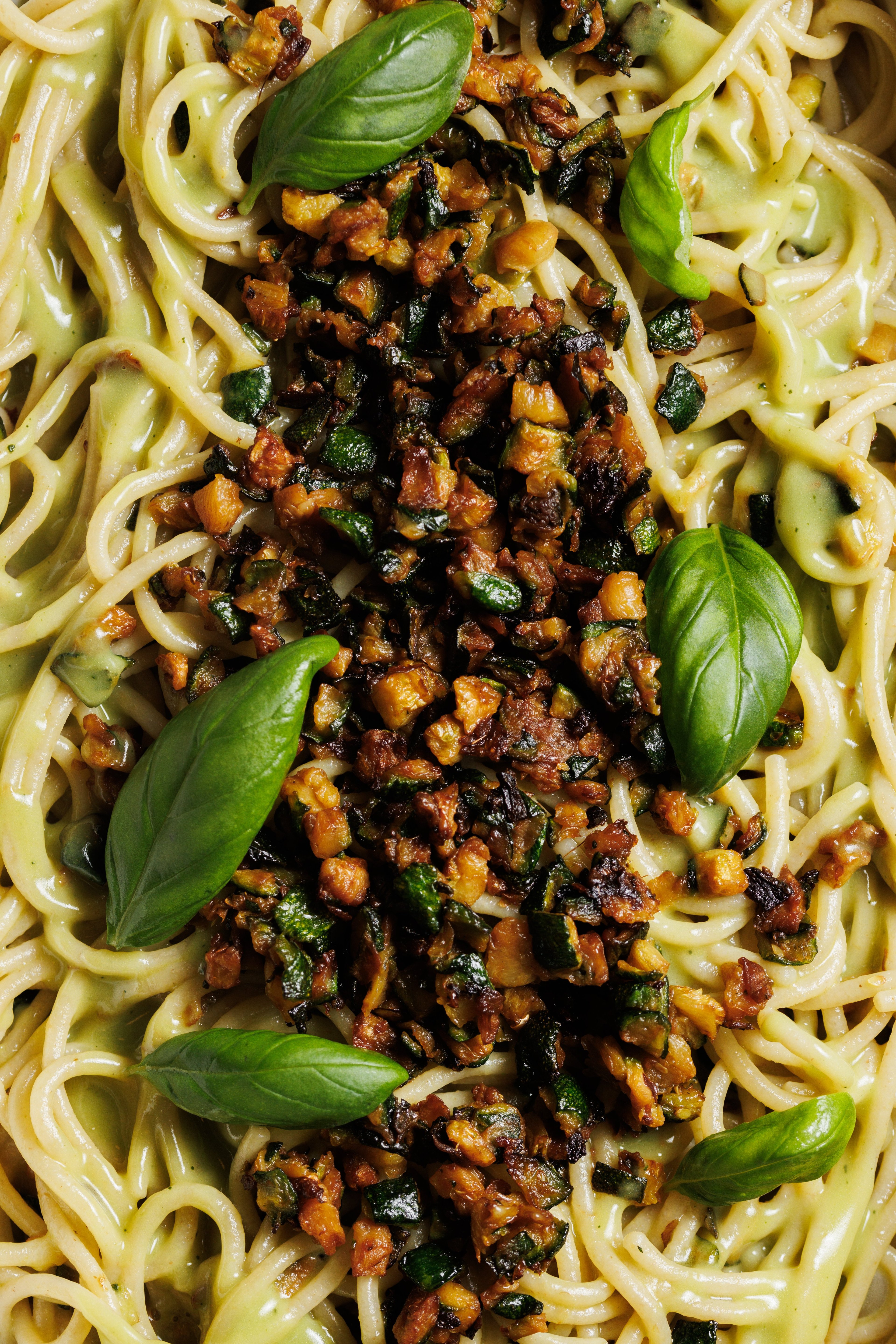 A close-up of creamy spaghetti topped with sautéed zucchini and fresh basil leaves.
