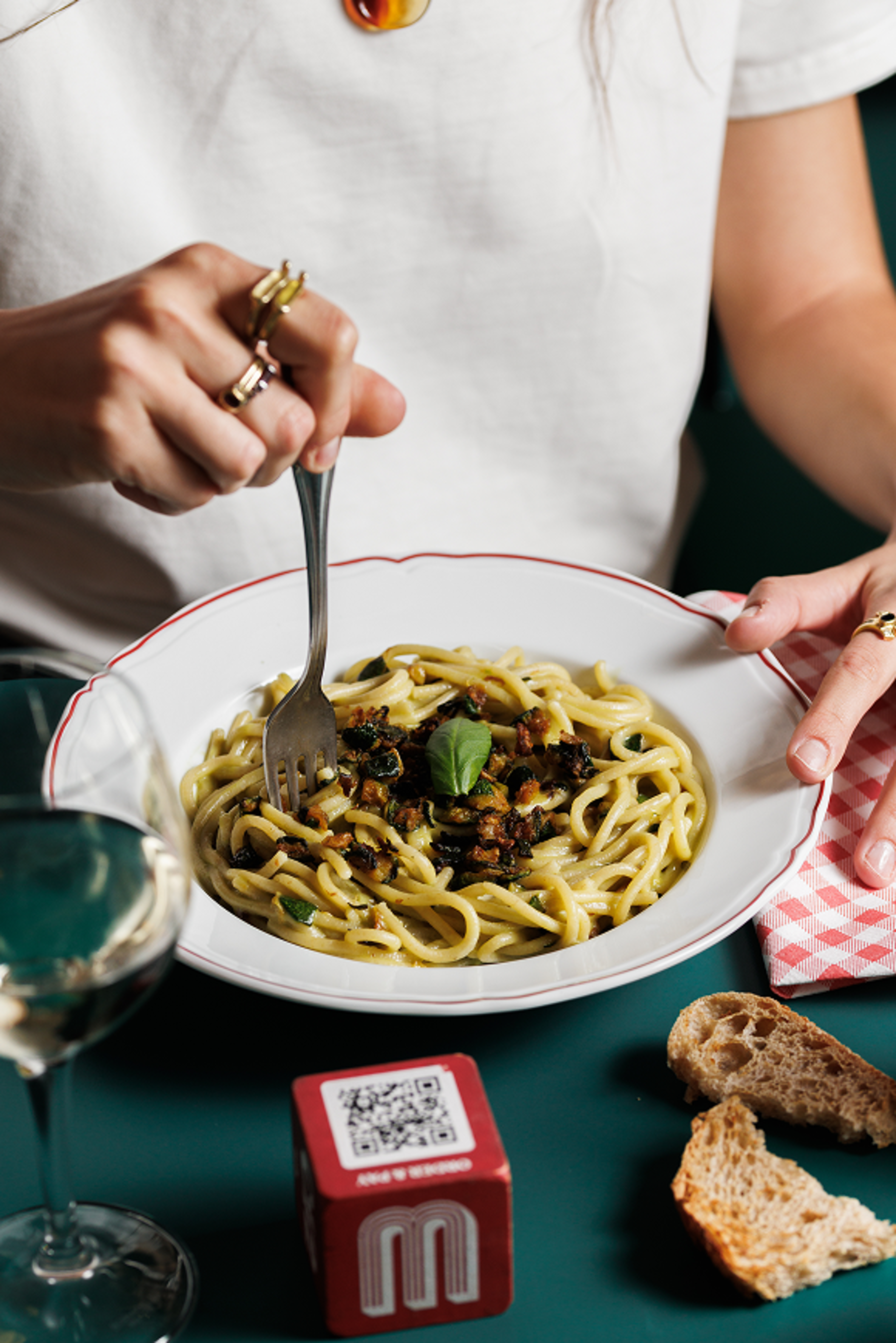 A person enjoys a plate of pasta with zucchini and herbs in a warmly lit restaurant setting.