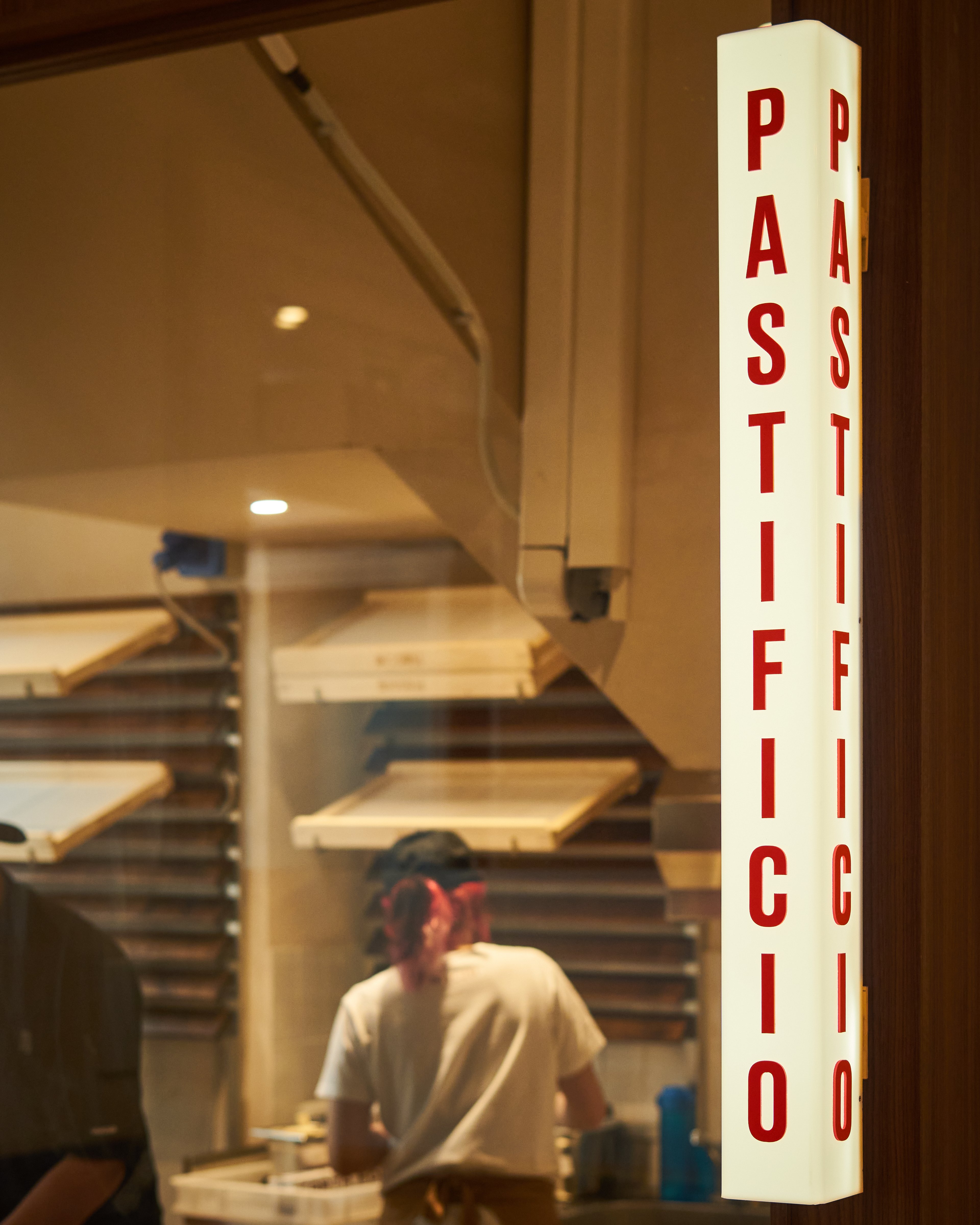 A person works in a brightly lit pasta shop with a vertical sign reading pastificio.