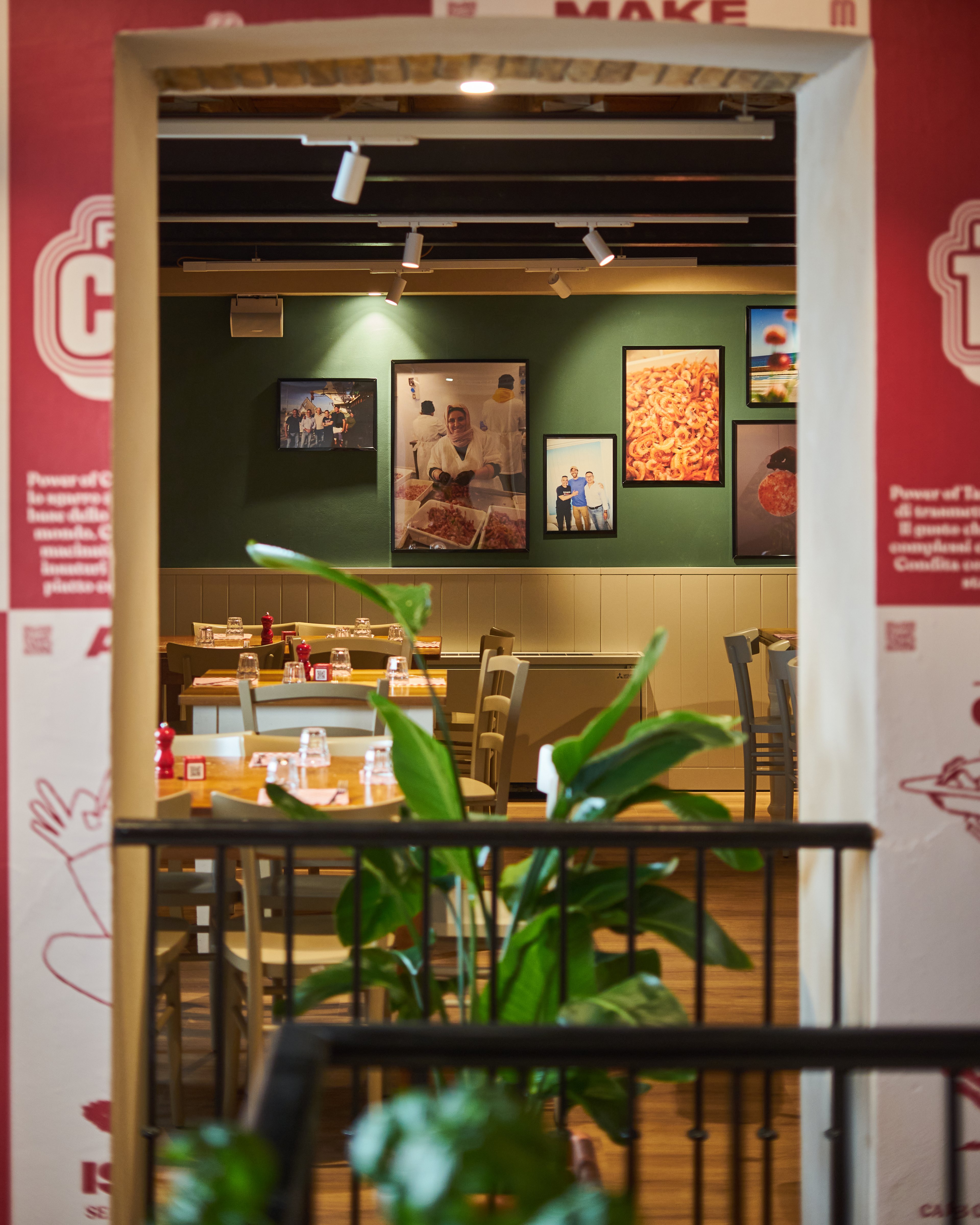 A cozy restaurant interior features warm lighting, framed food photography on a green wall, and neatly set dining tables.