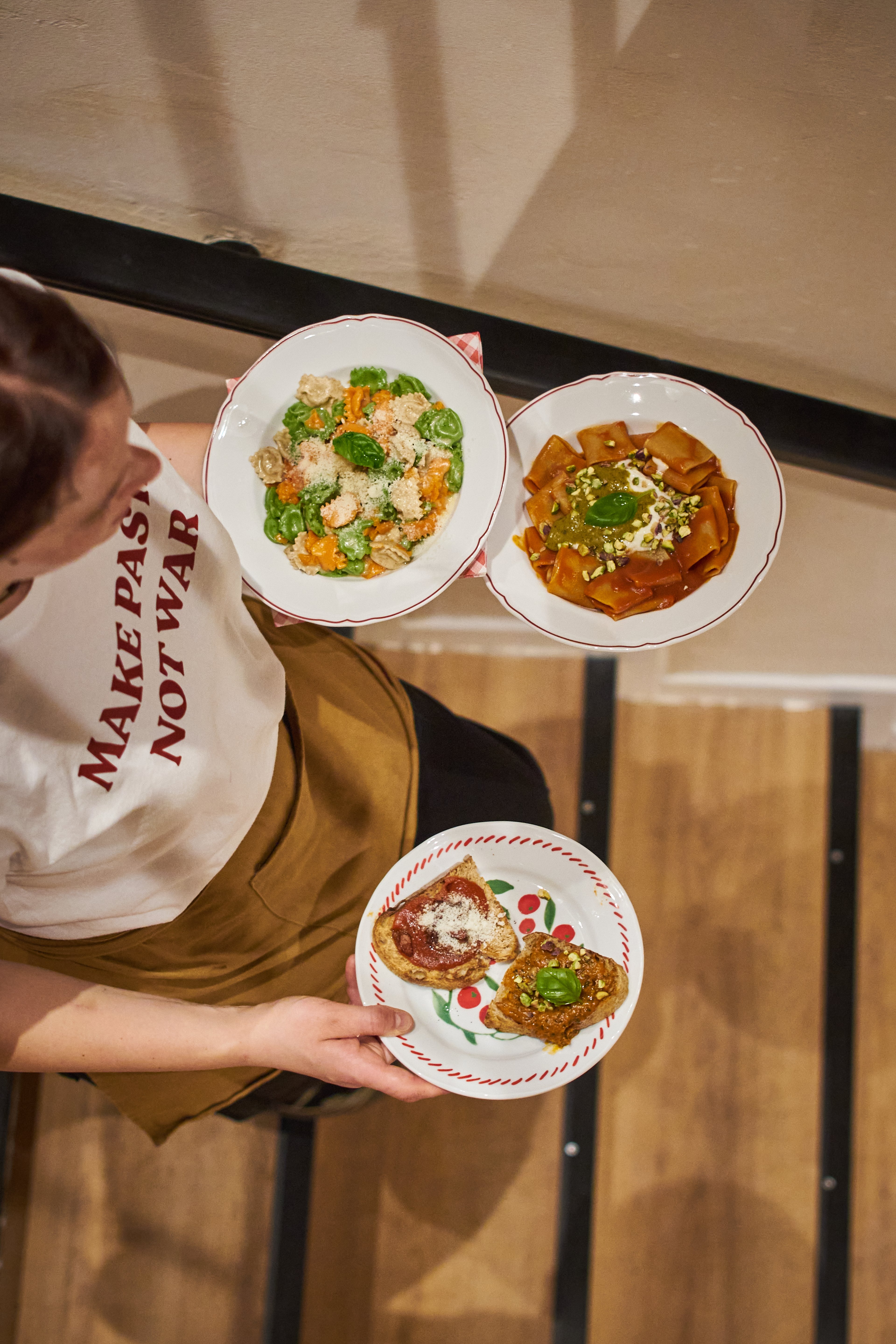 A server carries three plates of gourmet Italian pasta and bruschetta dishes in a warmly lit restaurant.