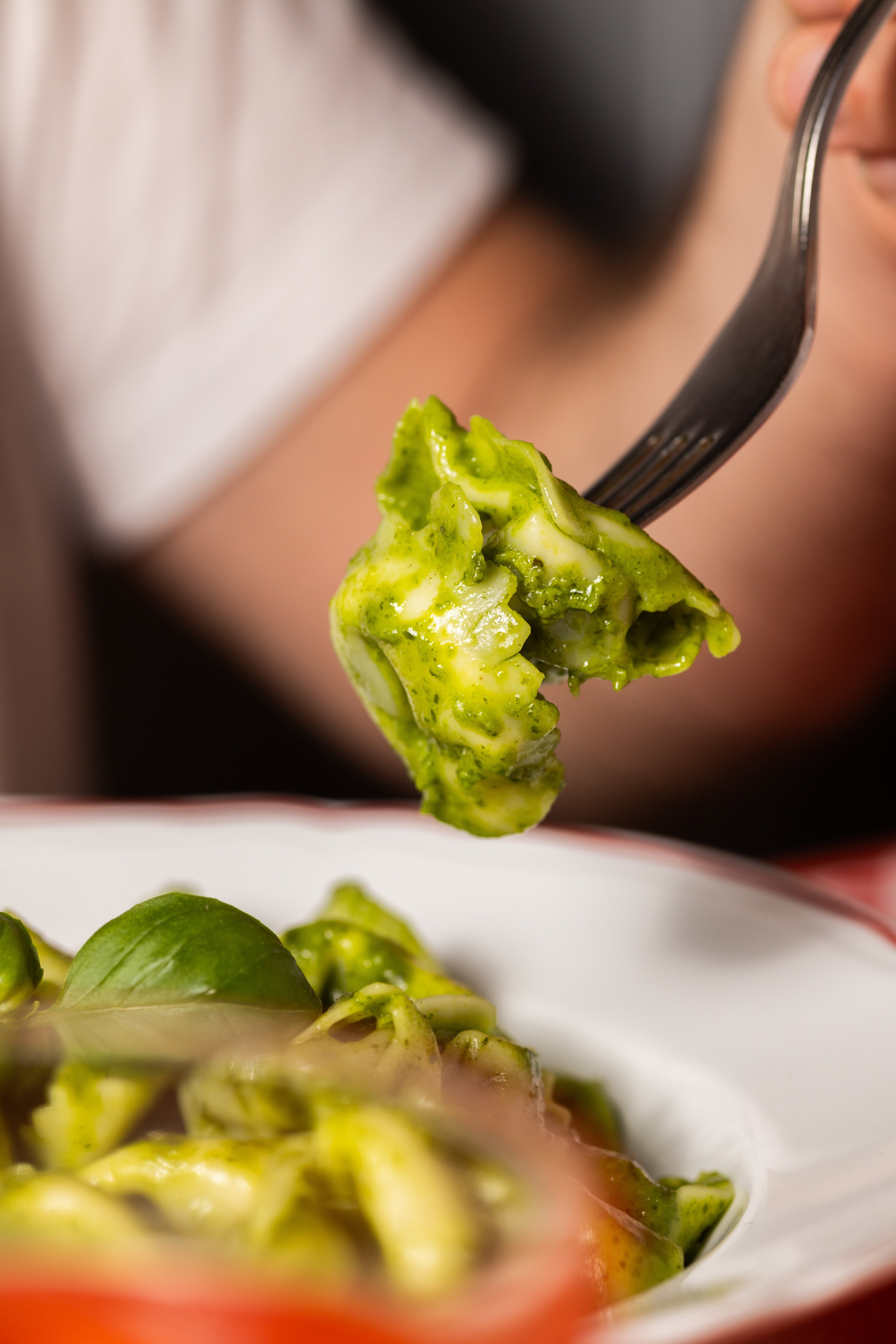 A close-up shot captures a fork lifting a piece of fresh tortellini coated in vibrant green pesto sauce.