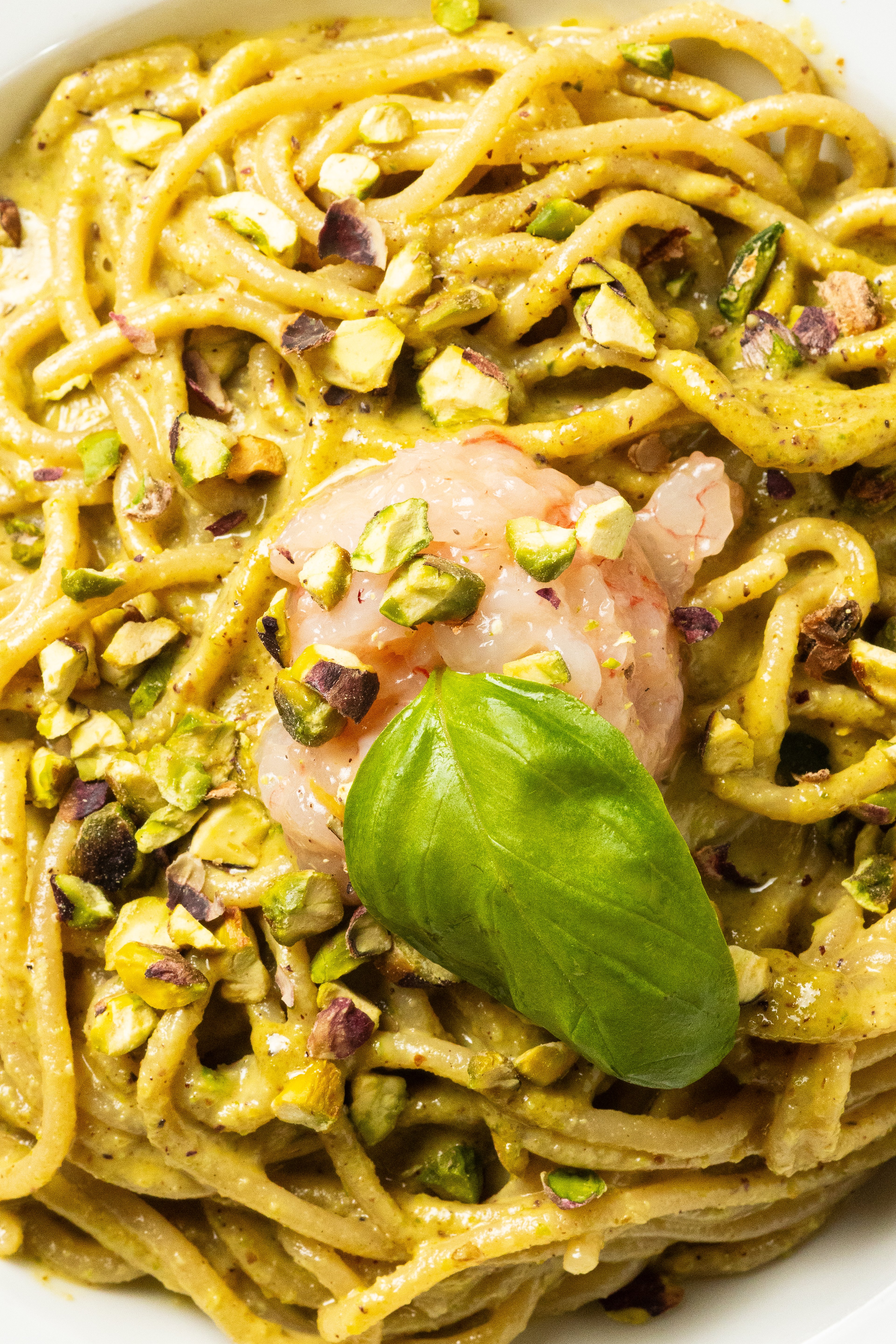 A close-up of a gourmet pasta dish featuring creamy pistachio sauce, fresh shrimp, and a basil garnish.