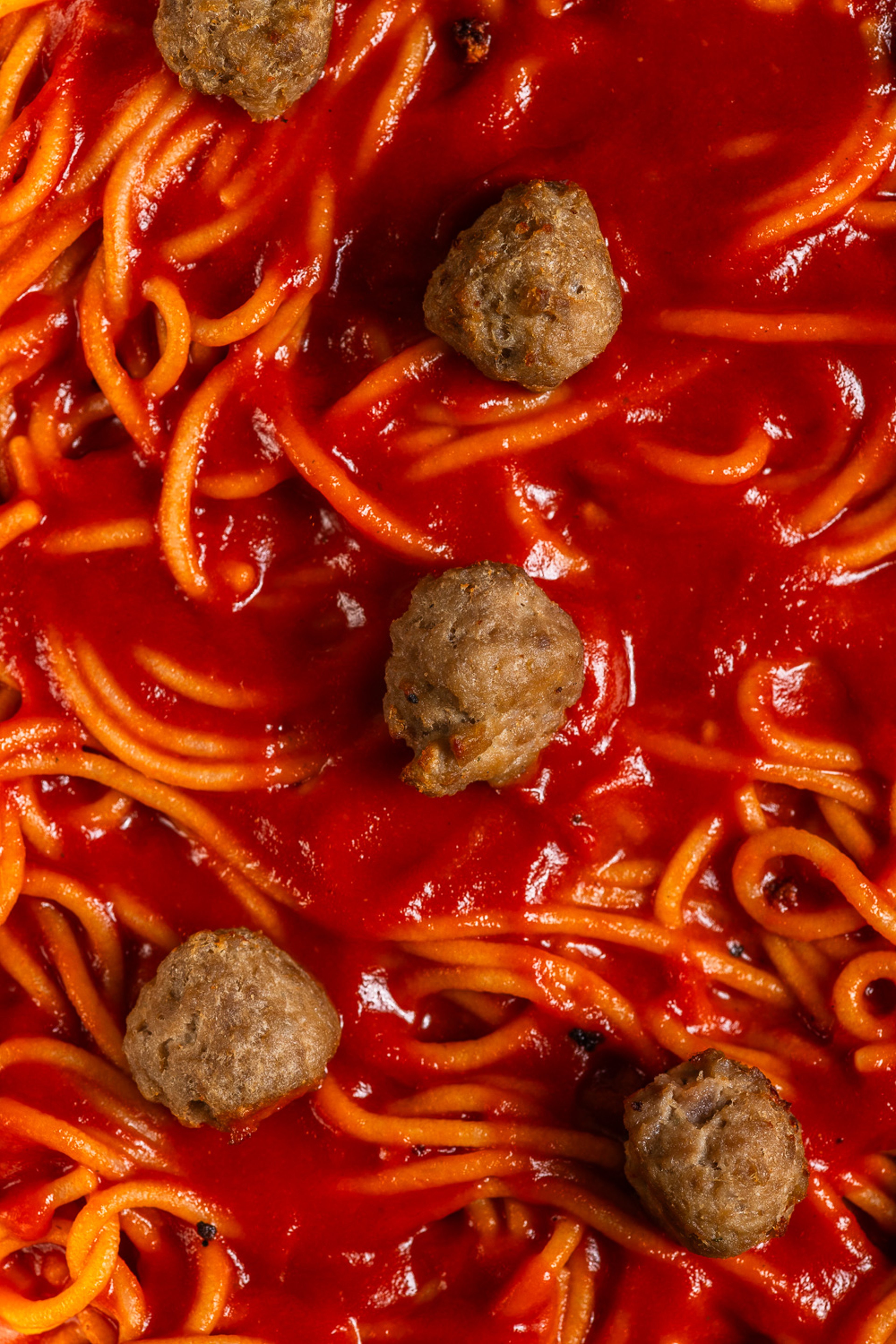A close-up view of spaghetti noodles coated in a rich red tomato sauce with several meatballs scattered throughout.
