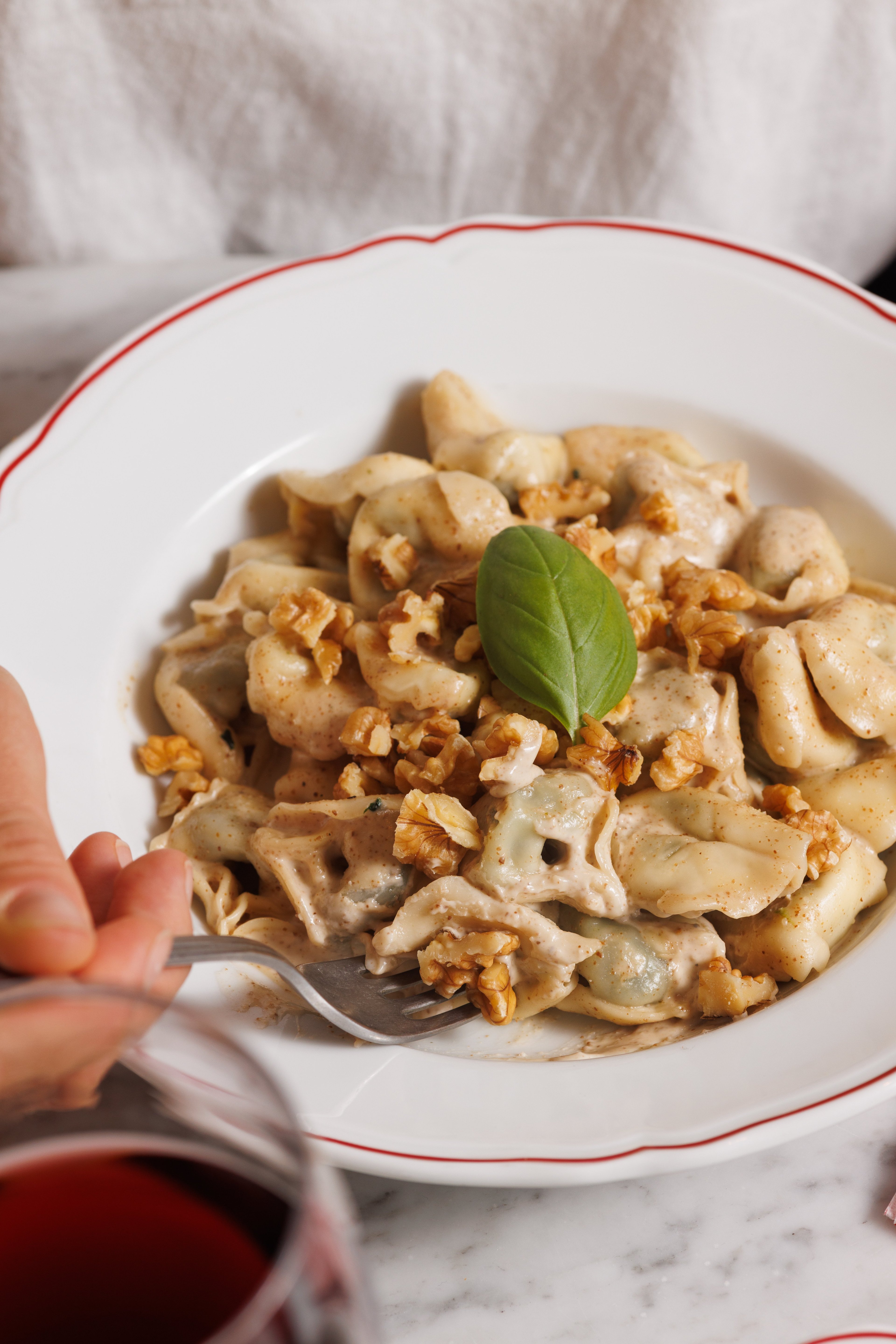 A close-up of a plate of creamy walnut tortellini garnished with a fresh basil leaf.