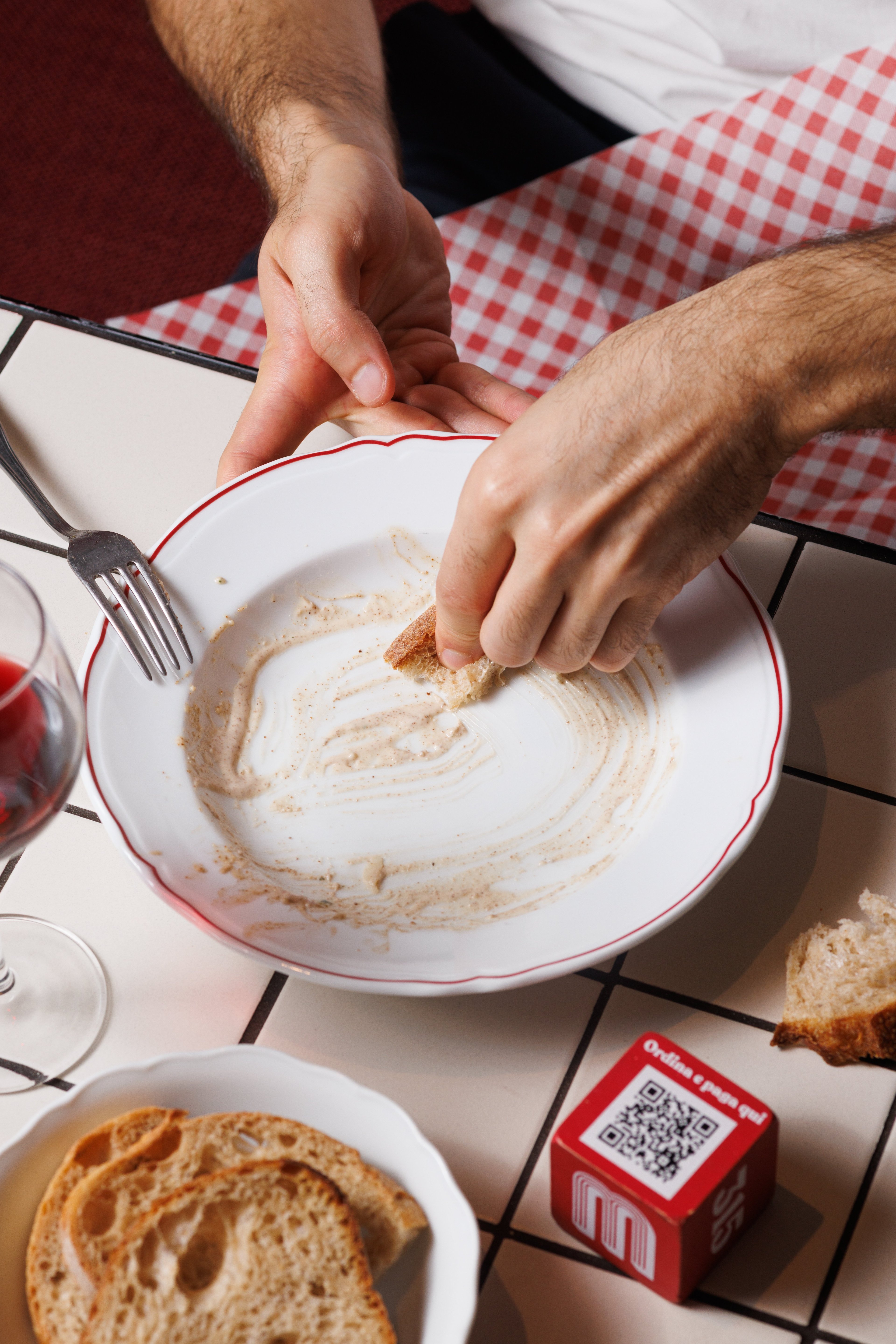 A person uses a piece of bread to wipe the remaining sauce from a plate at a restaurant table.