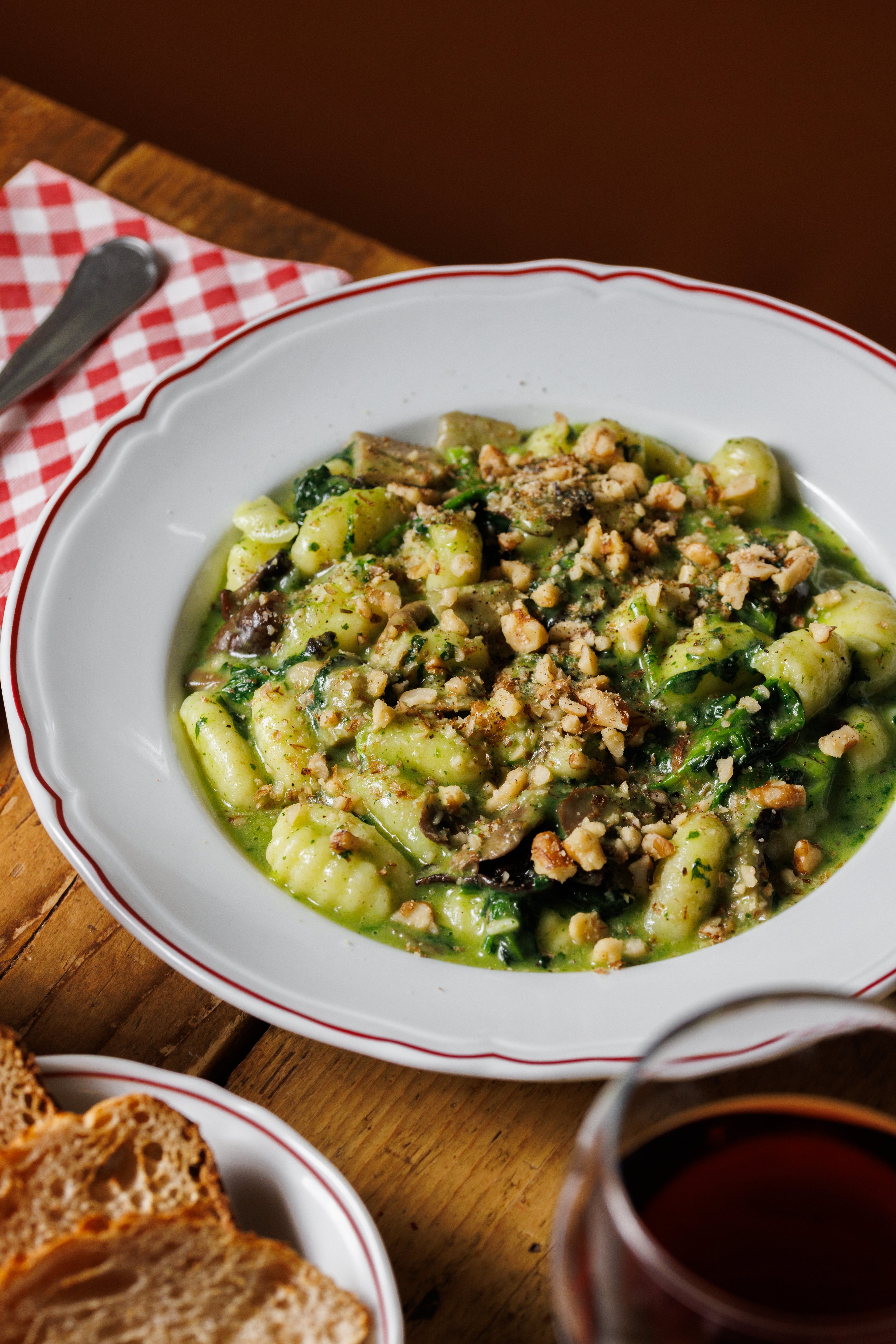 A rustic plate of gnocchi with spinach, mushrooms, and walnuts served on a wooden table.
