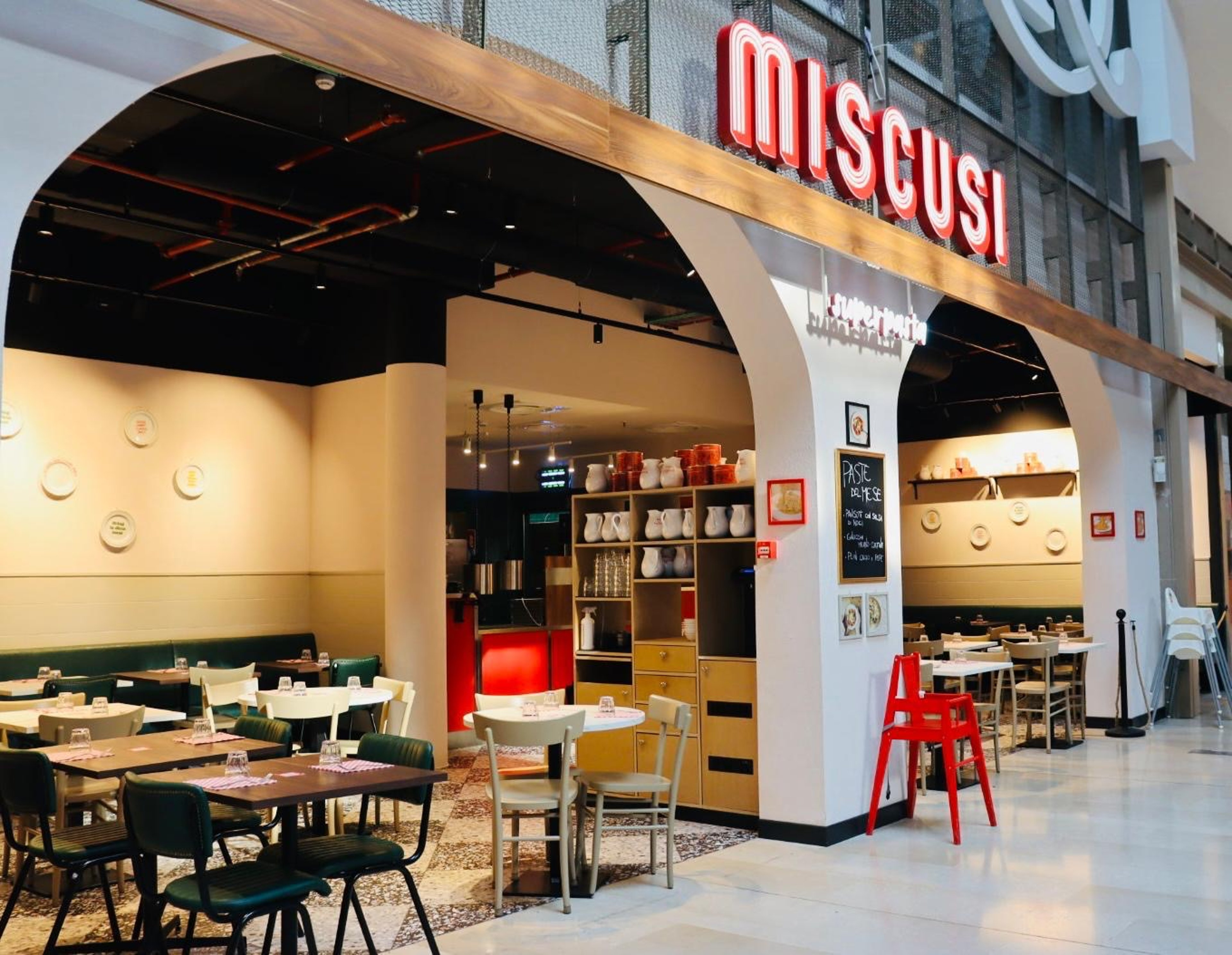 A warmly lit Italian-style restaurant with neatly arranged tables, chairs, pottery, and a chalkboard menu.