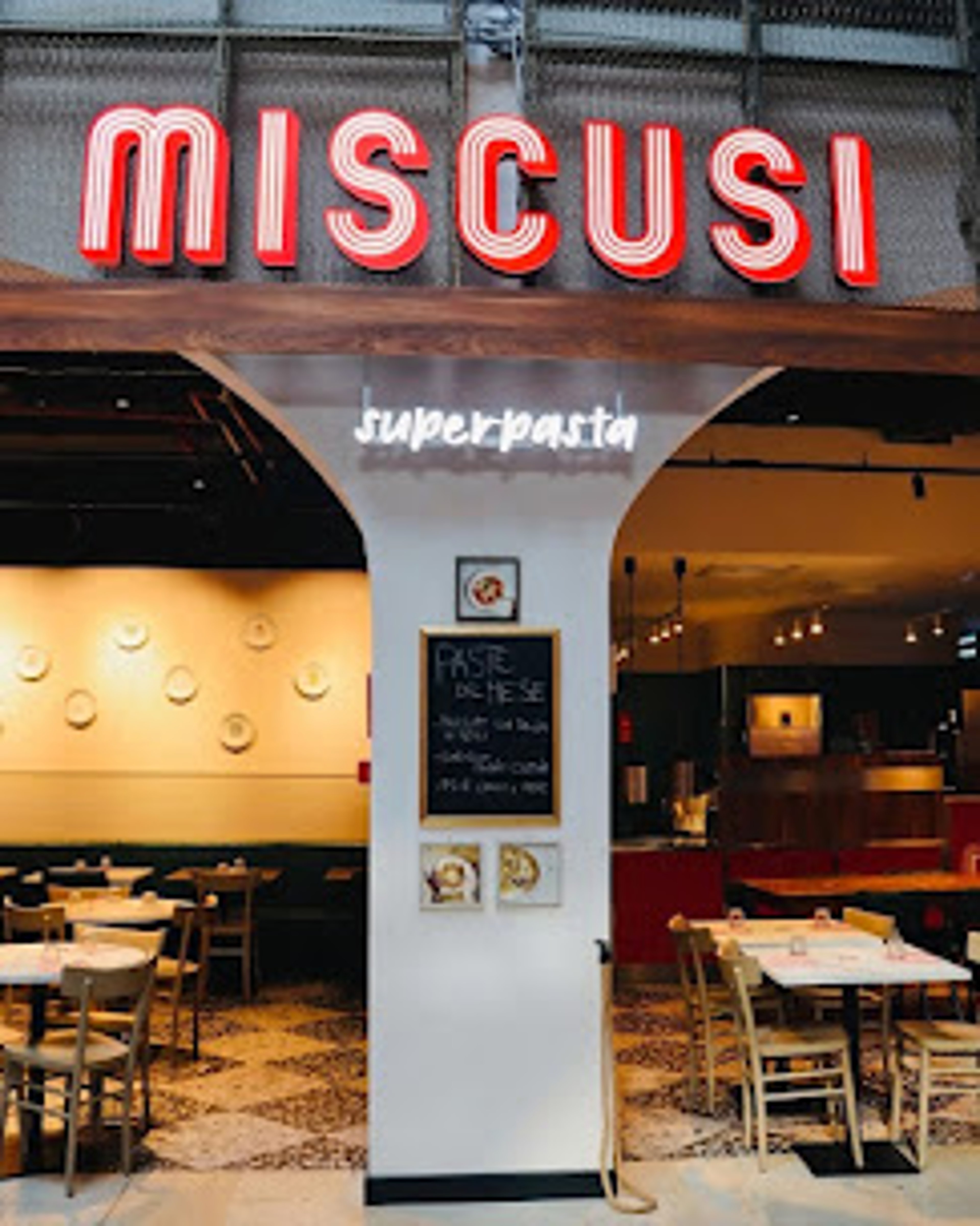 An open Italian-style restaurant has empty tables, a bar, and warm interior lighting beneath a glowing sign.